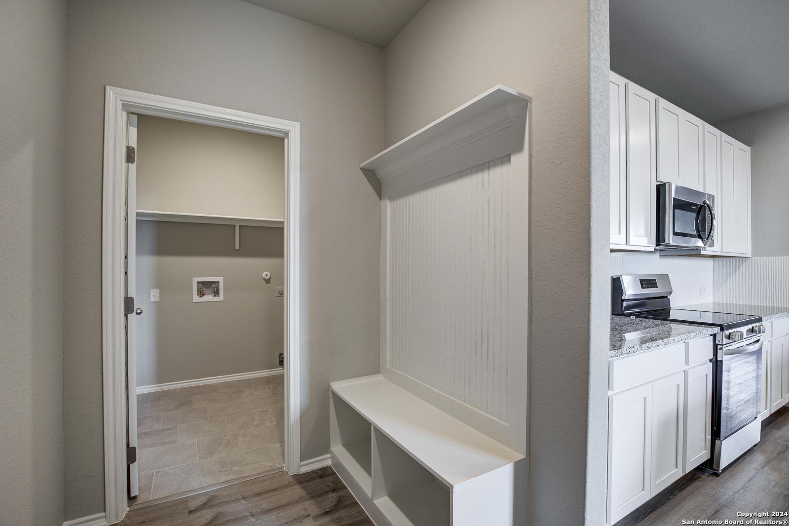Mudroom with shiplap bench, coat hooks, and adjacent laundry room next to white cabinet kitchen in Davidson Homes The Blanco C, San Antonio