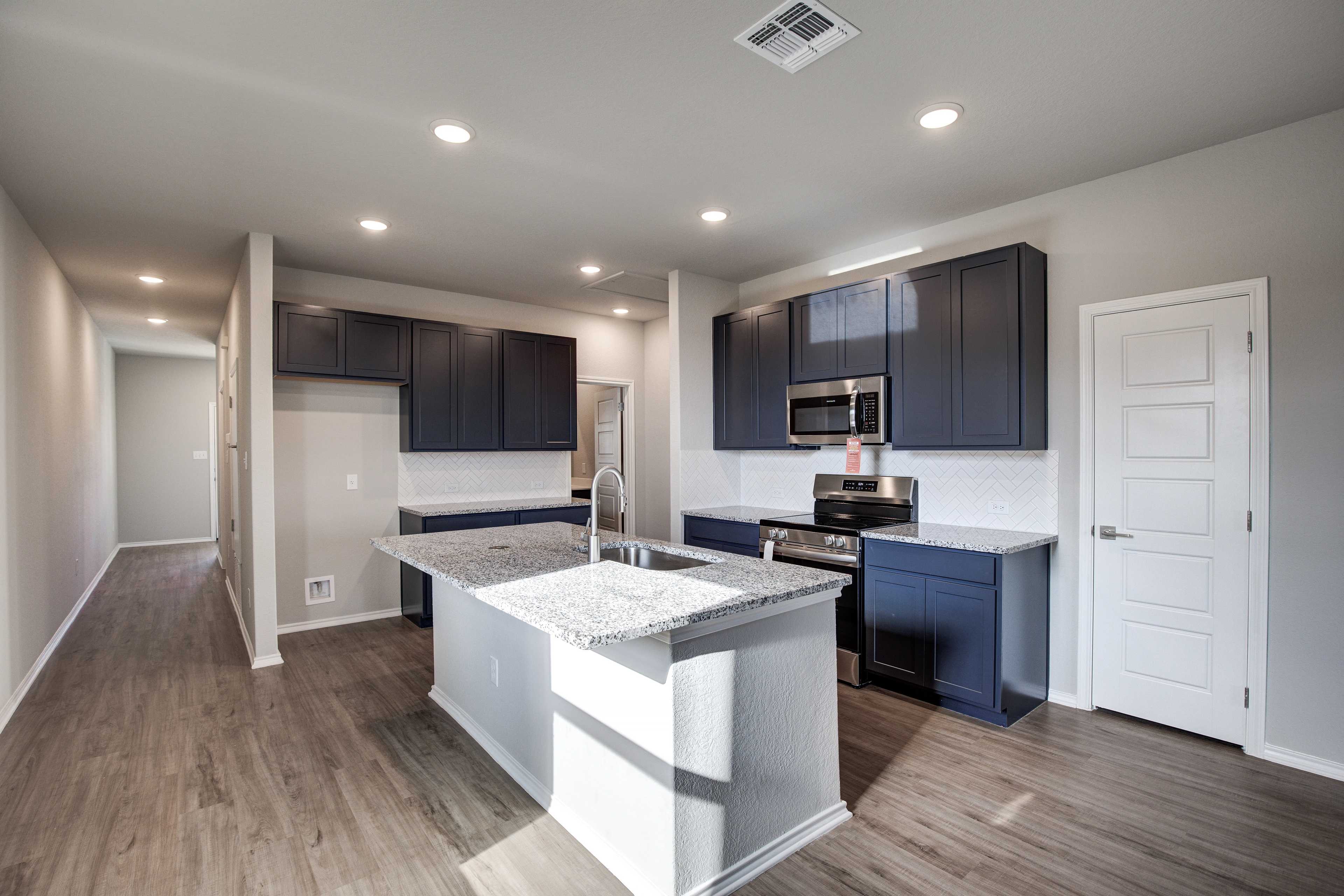 Modern kitchen in The Frio B by Davidson Homes featuring navy cabinets, granite island sink, stainless appliances, open layout