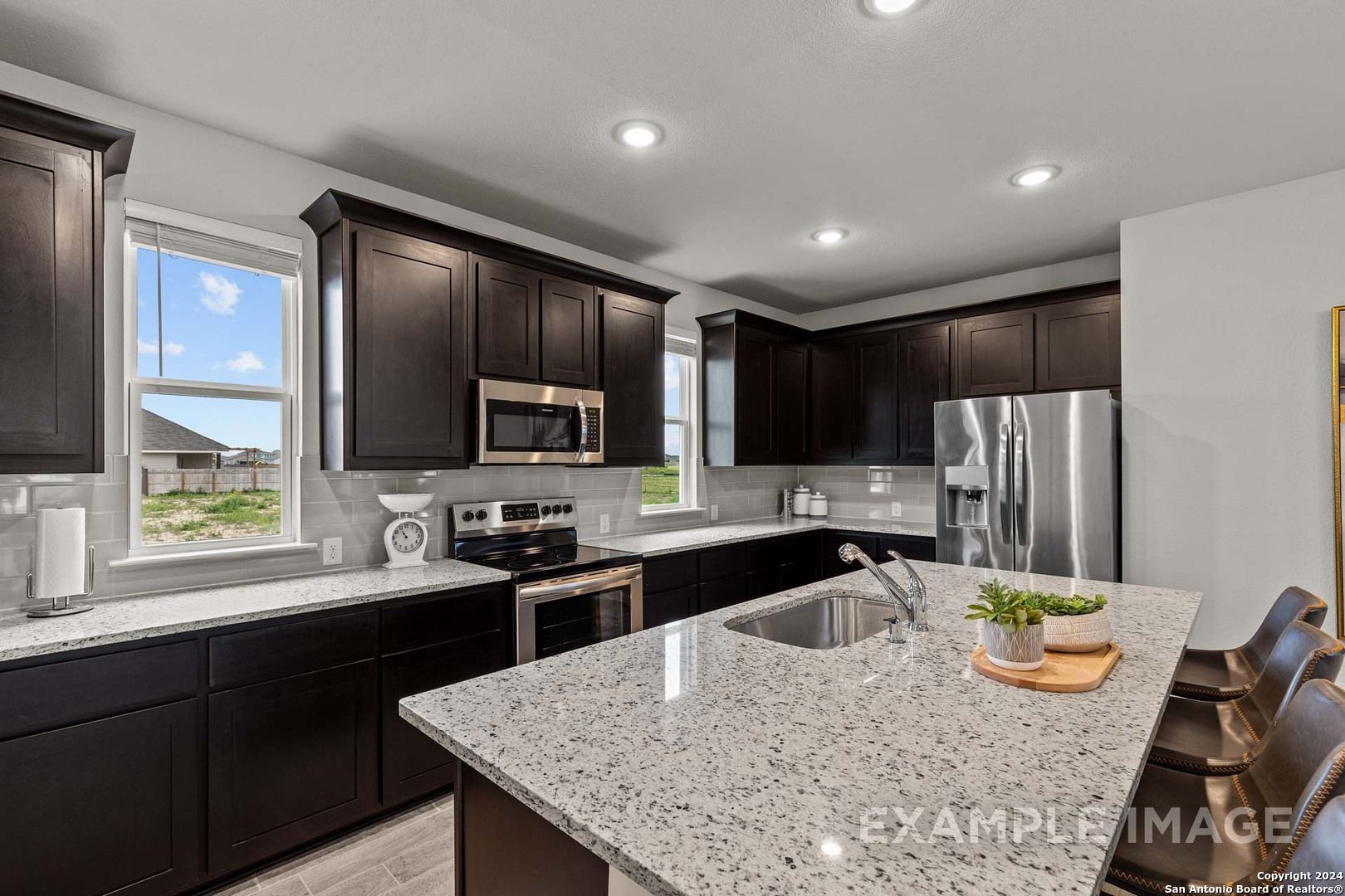 Modern kitchen with dark shaker cabinets, granite countertops, stainless appliances, and island seating in The Collin A, Seguin TX