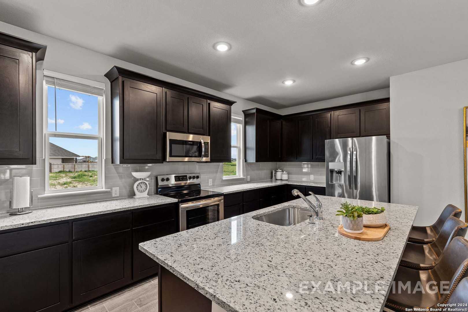 Modern kitchen with dark shaker cabinets, granite countertops, stainless appliances, and island seating in The Collin A, Seguin TX