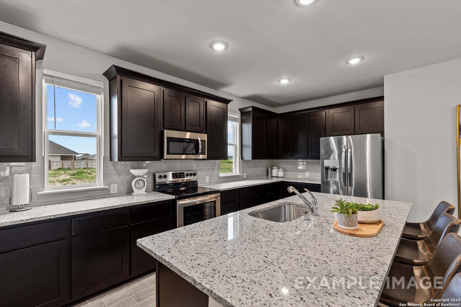 Modern kitchen with dark shaker cabinets, granite countertops, stainless appliances, and island seating in The Collin A, Seguin TX