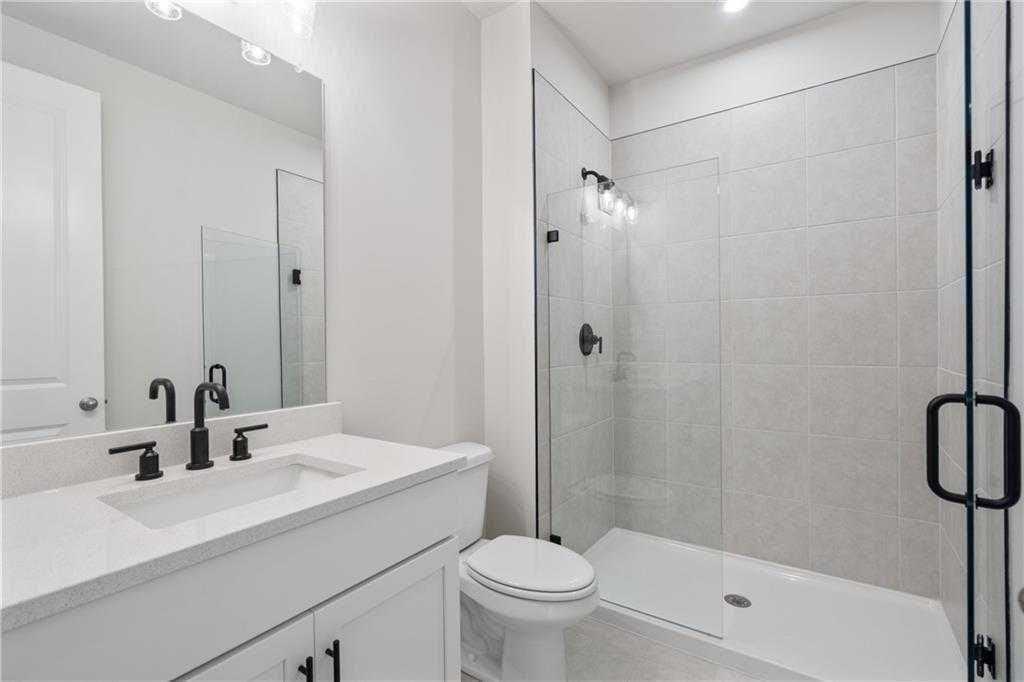 Modern white bathroom with frameless glass shower, single vanity sink, and toilet in 5-bedroom Davidson Homes The Hickory B, Buford, GA