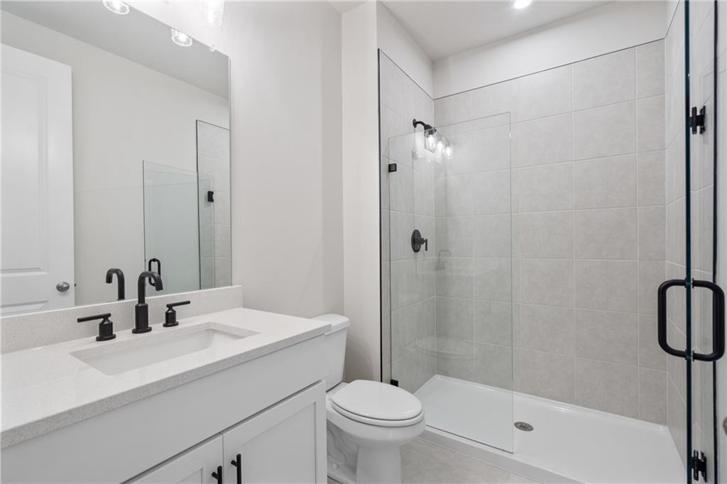 Modern primary bathroom with white quartz vanity, black faucets, frameless glass shower, and subway tiles in Davidson Homes Hickory E, Buford, GA