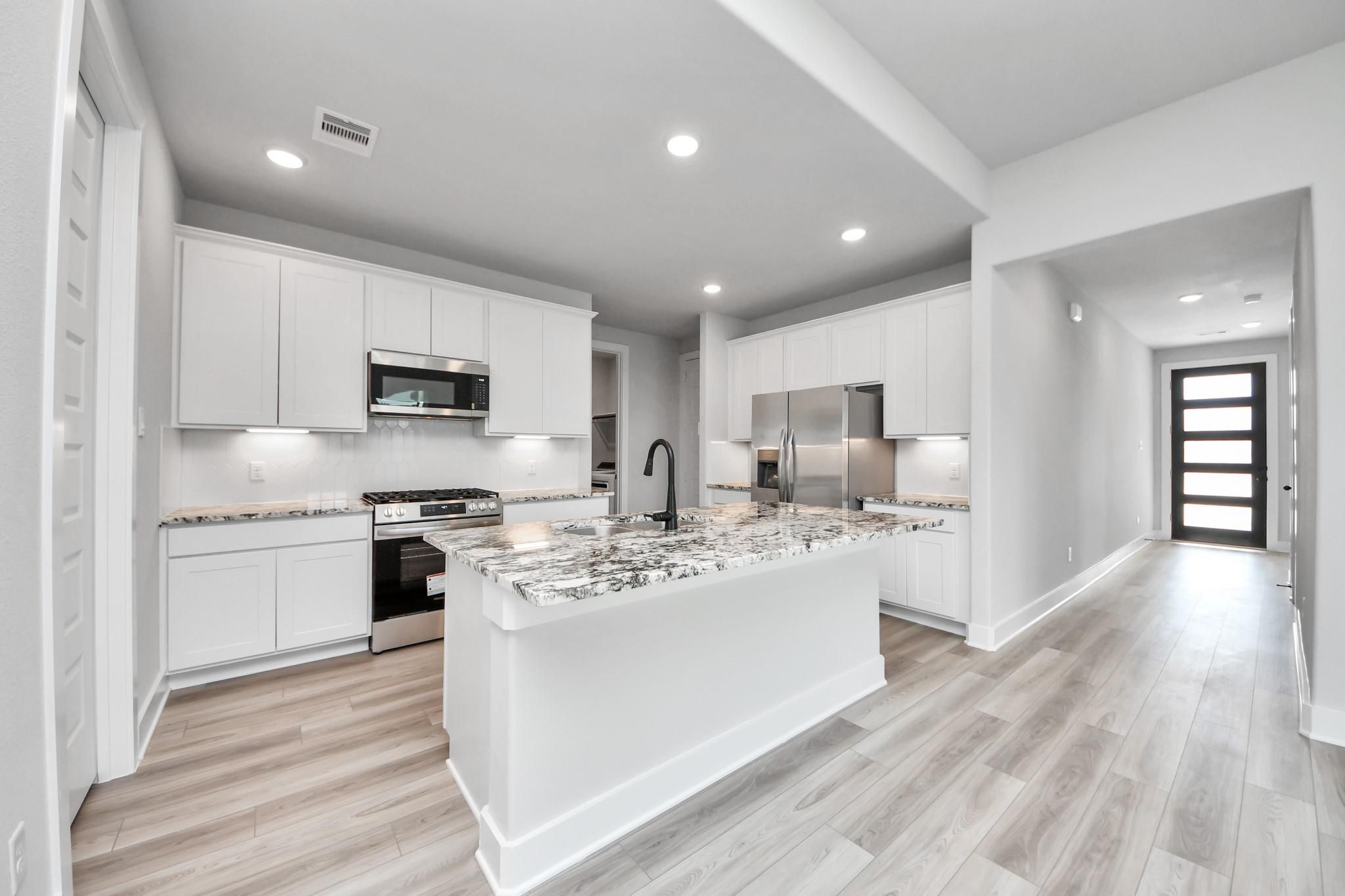 Modern kitchen with white cabinets, granite island, and stainless appliances in The Laguna C floor plan, Sunterra, Katy.