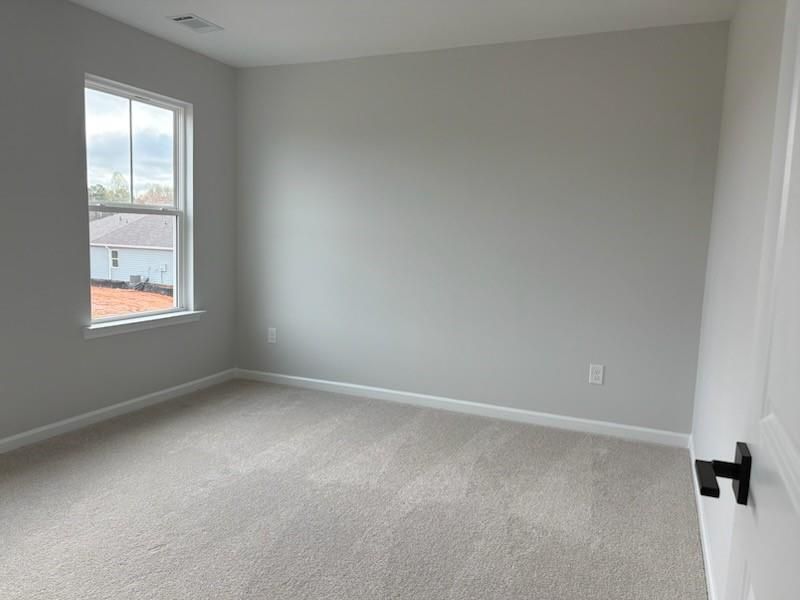 Empty bedroom with light gray walls, neutral carpet, and large window in Davidson Homes The Hickory B, Winder, Georgia