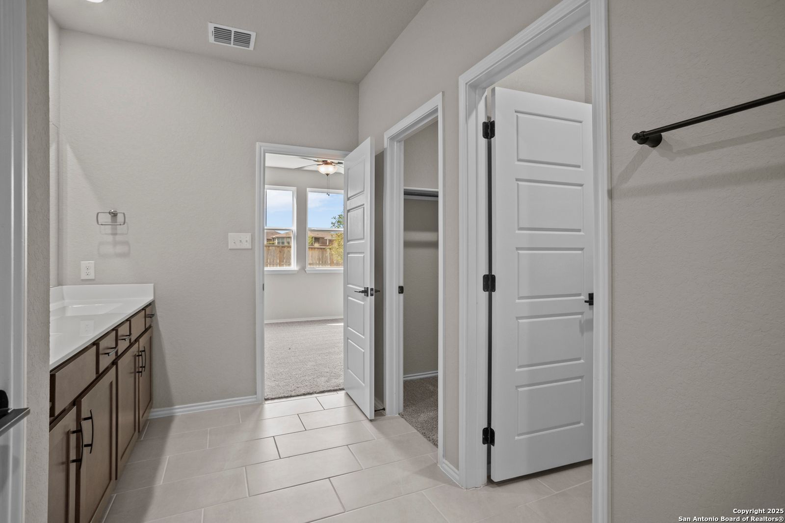 Modern master bathroom with vanity sink, tiled floors, and open doors to walk-in closet and bedroom in Davidson Homes The Douglas F, San Antonio