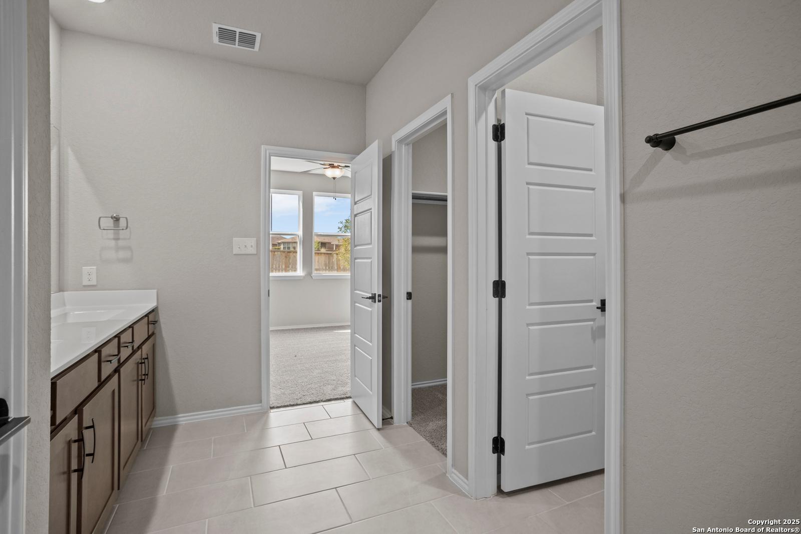 Modern master bathroom with vanity sink, tiled floors, and open doors to walk-in closet and bedroom in Davidson Homes The Douglas F, San Antonio