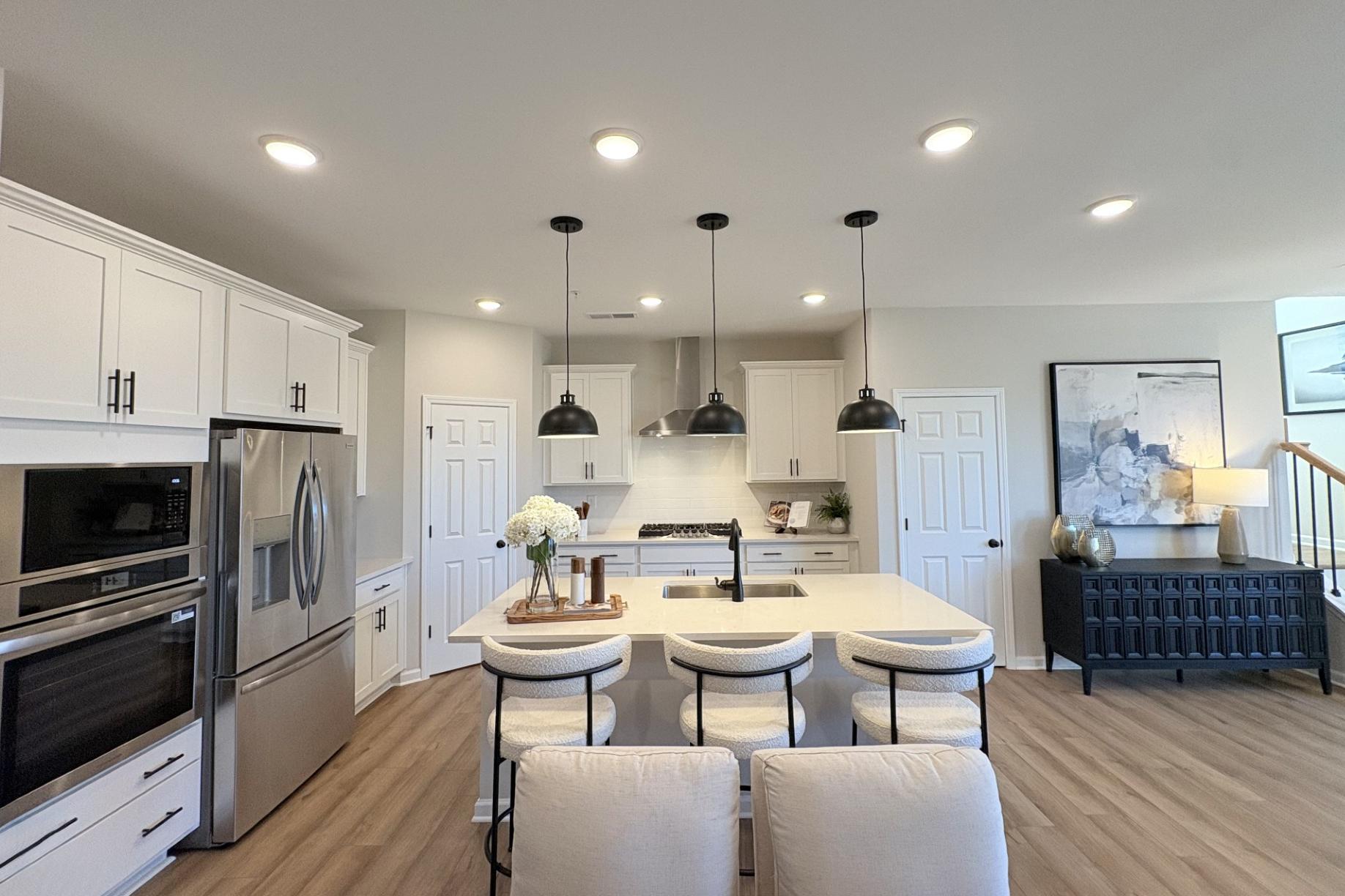 Modern kitchen in Hemingway Cumming GA with white shaker cabinets, quartz island, stainless appliances, pendant lights and hardwood floors