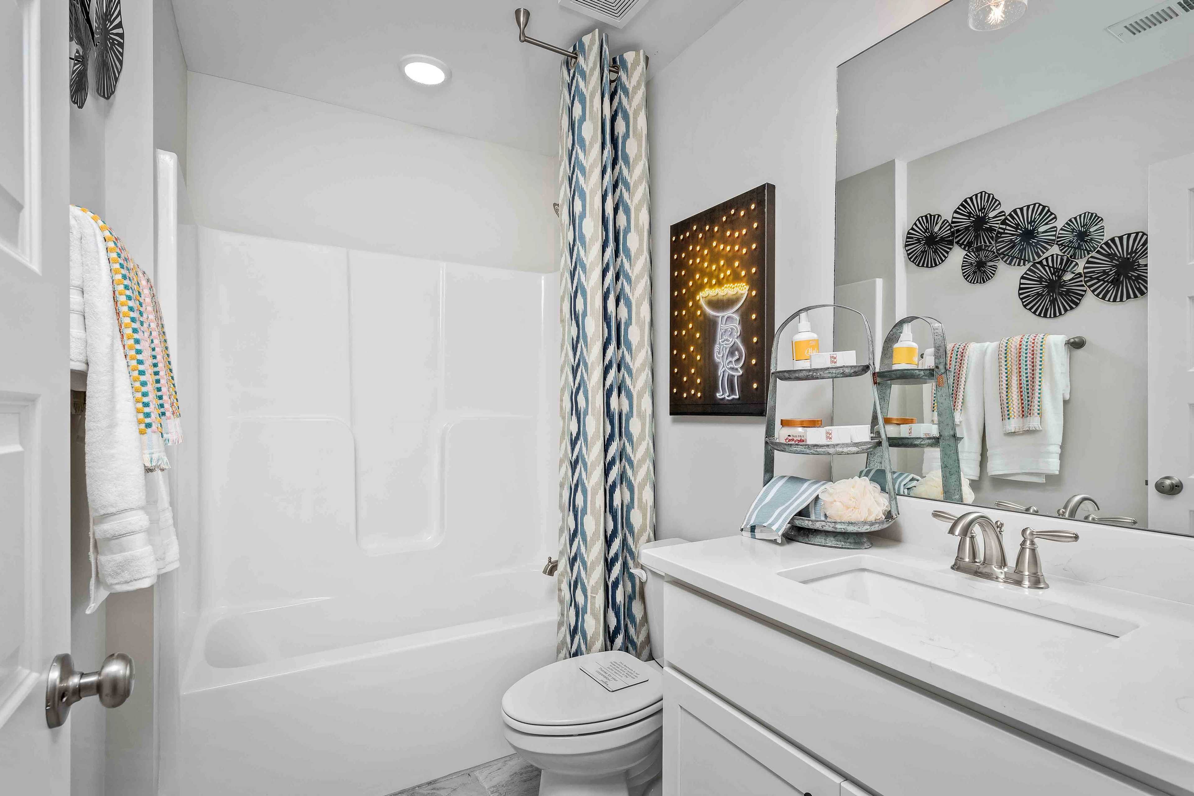 Modern bathroom at Cain Park in Hartselle, Alabama with white tub, vanity sink, blue shower curtain and yellow star artwork