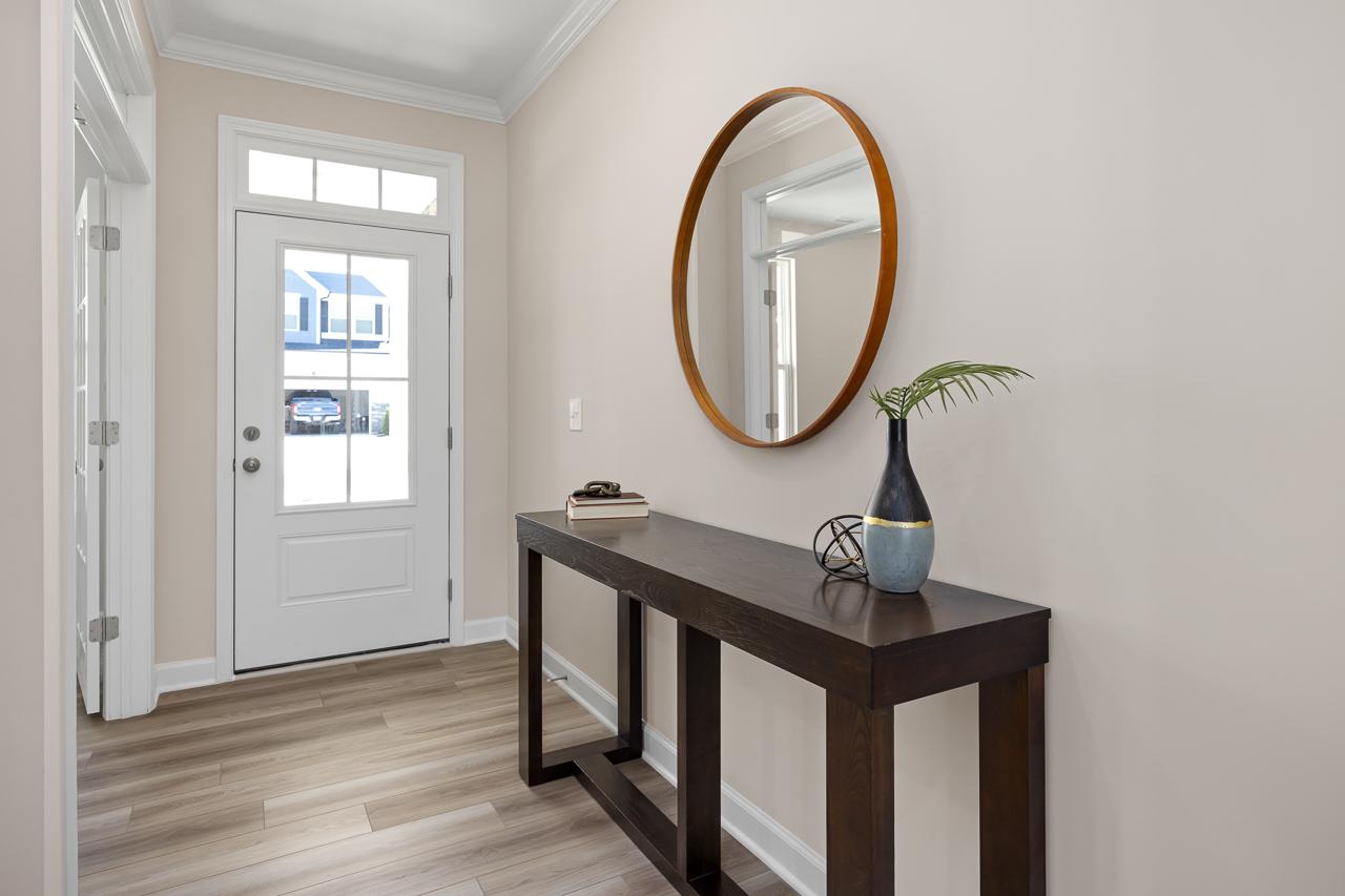 Bright entryway of The Chestnut by Davidson Homes featuring a modern console table, round wall mirror, and wood flooring.