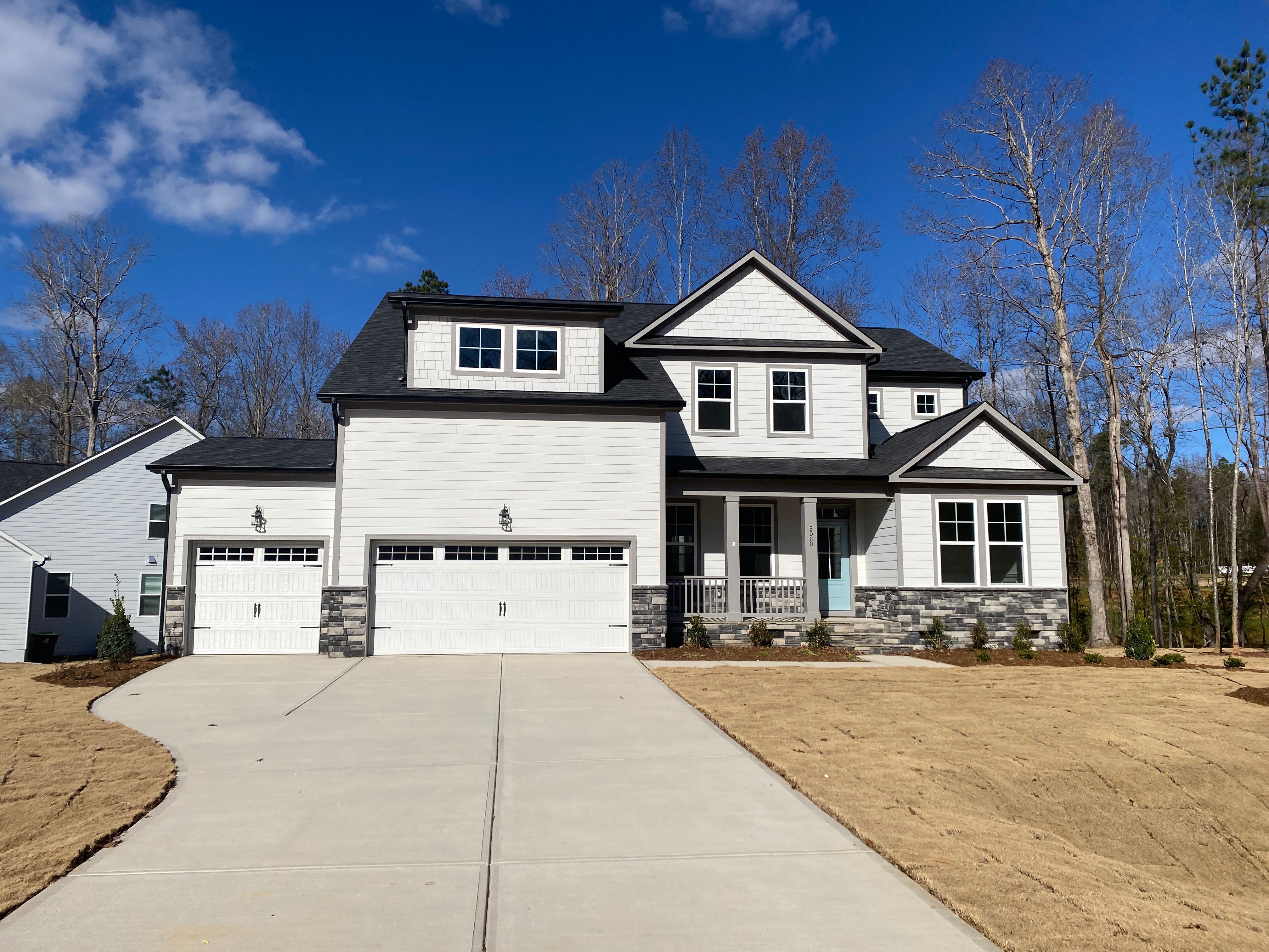 Sage green Craftsman home exterior at Ashland in Apex NC with covered front porch, two-car garage, and wooded backdrop