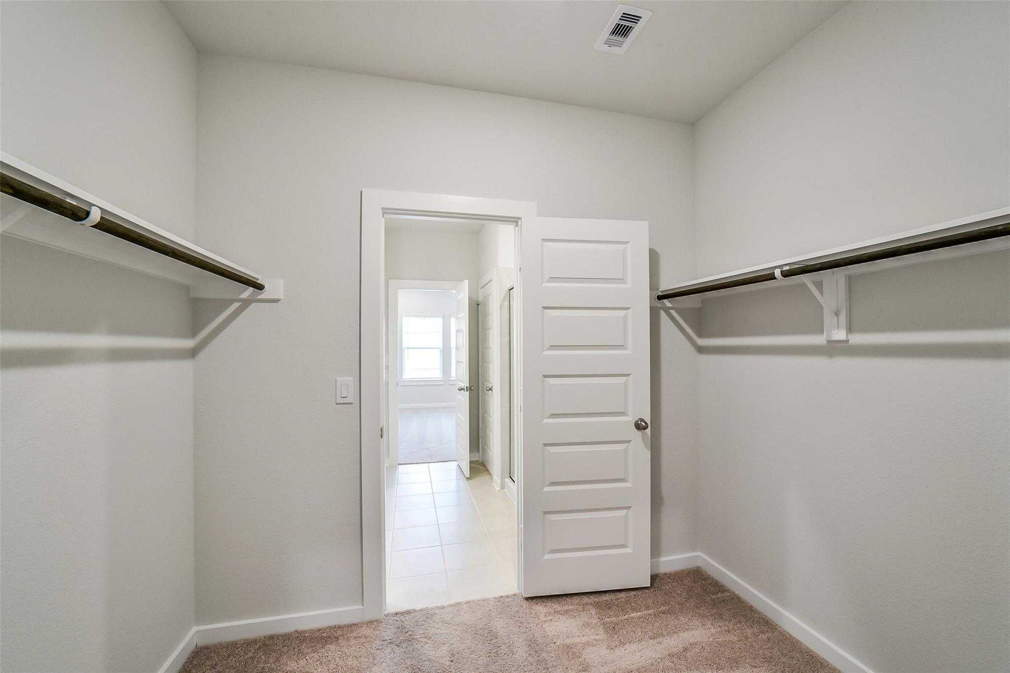 Spacious walk-in closet with double hanging rods and open door to master bath in Davidson Homes Blanco E, Magnolia, Texas
