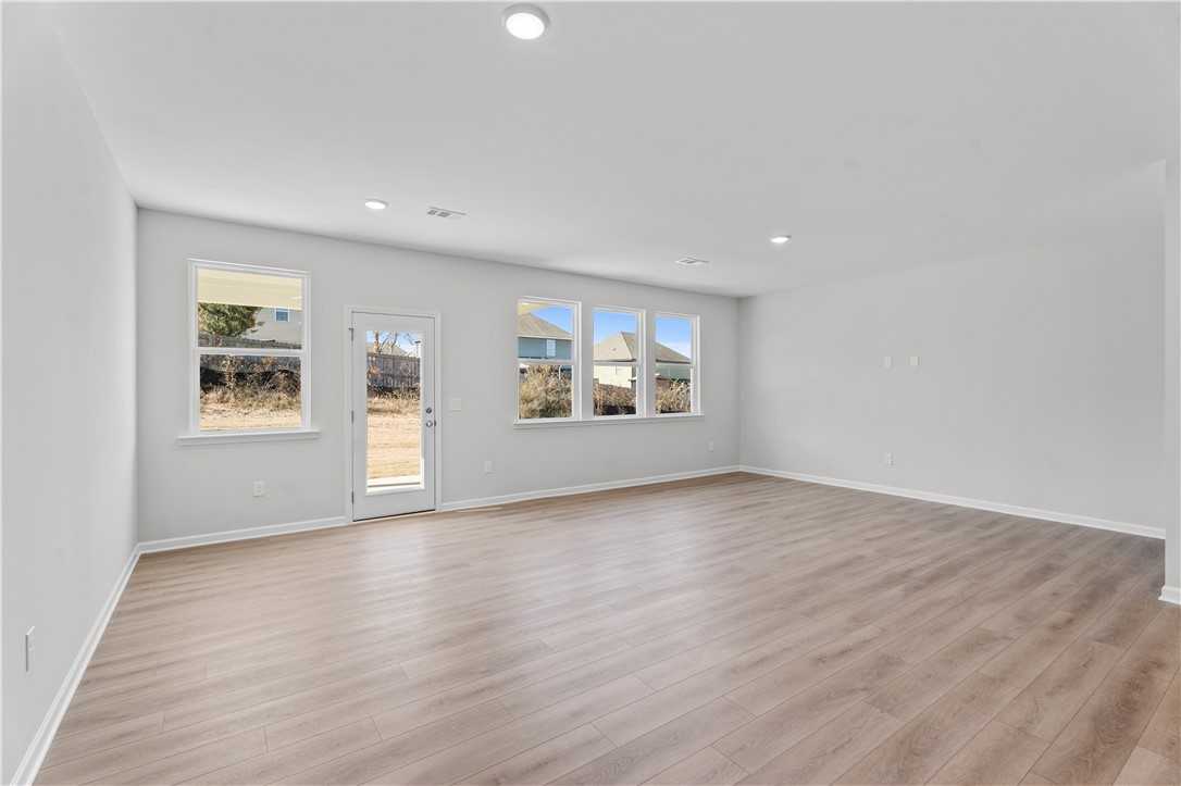 Spacious empty living room with light hardwood floors, white walls, large windows, and sliding glass door to backyard in The Luna B 4-bedroom home, Opelika, Alabama