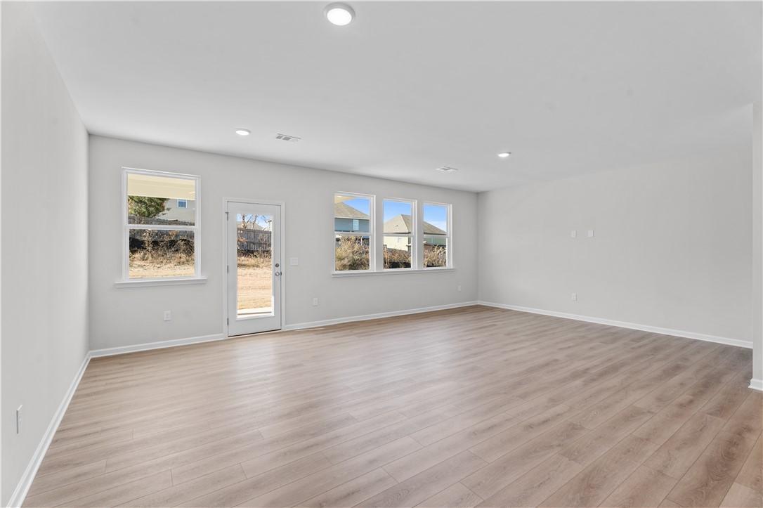 Spacious empty living room with light hardwood floors, white walls, large windows, and sliding glass door to backyard in The Luna B 4-bedroom home, Opelika, Alabama