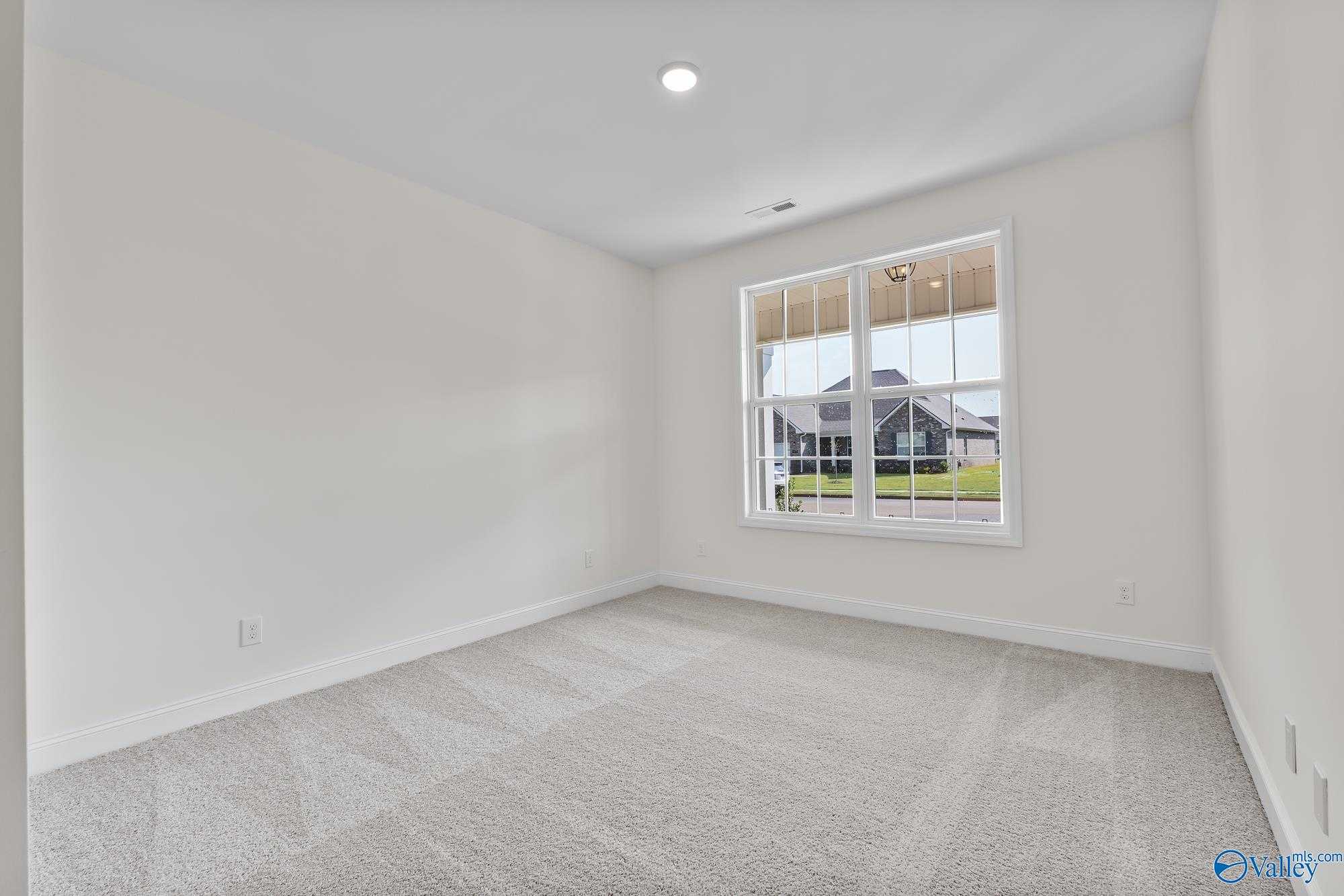 Bright empty bedroom with white walls, neutral carpet, and large window overlooking lawn in The Harrison, Meridianville, AL