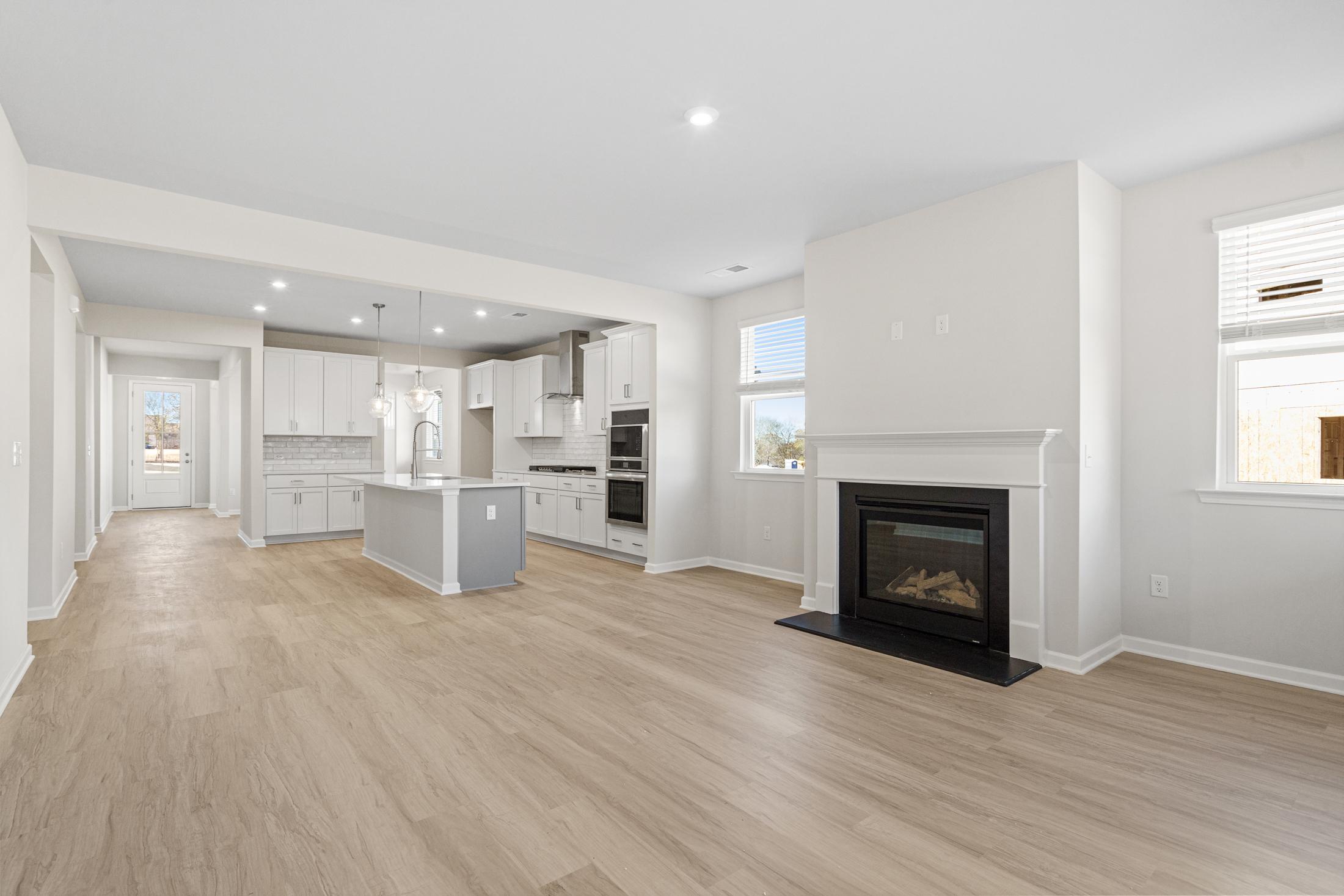 Spacious open-concept kitchen and great room in The Glenwood A featuring white cabinetry, large center island, gas fireplace, and oak hardwood floors