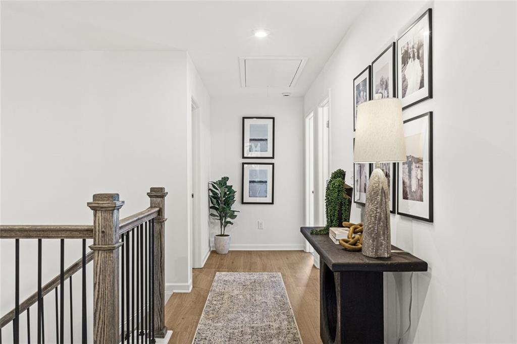 Bright upstairs hallway with hardwood floors, runner rug, wooden balustrade, and modern console in The Hickory B home, Hoschton, GA