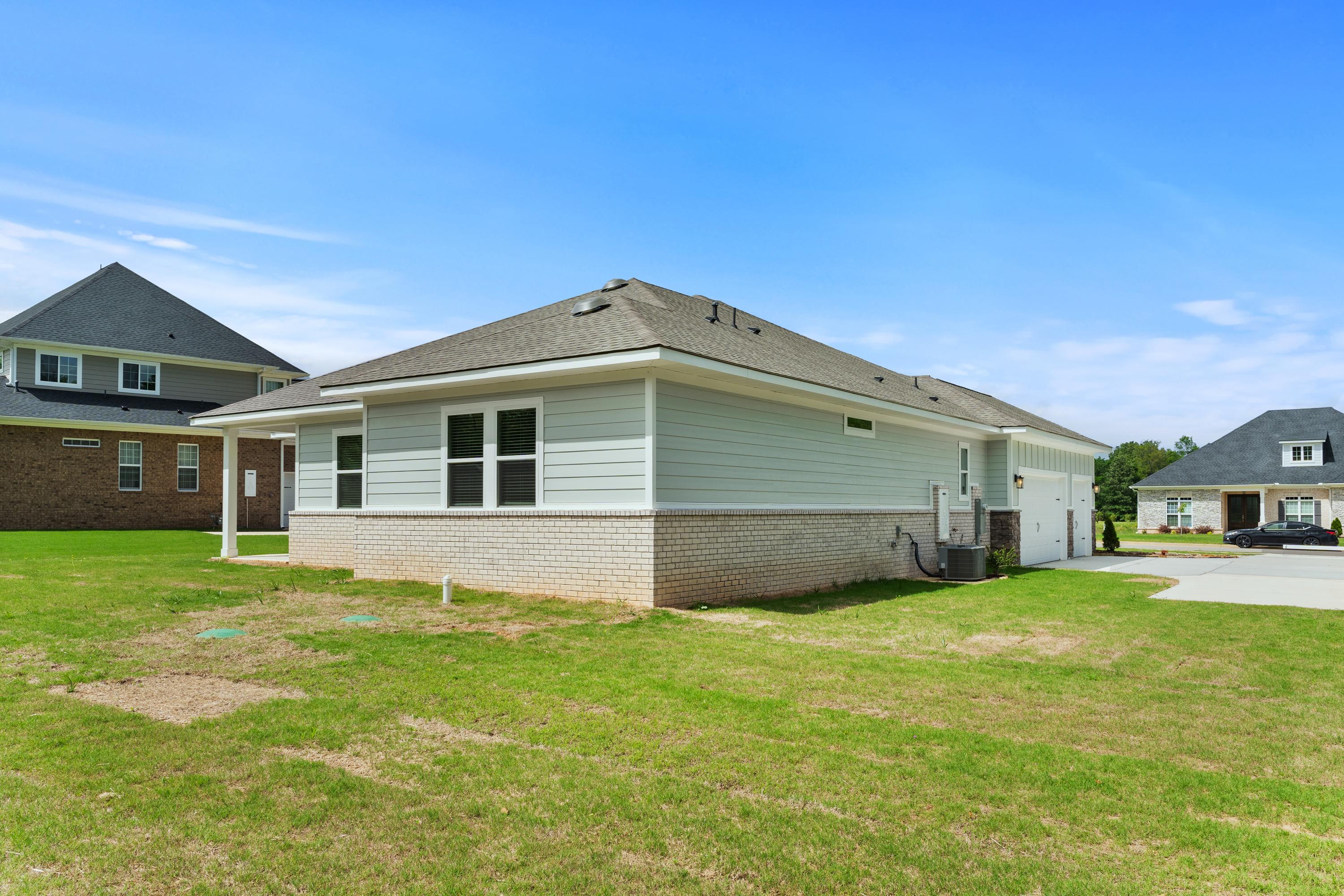 Side elevation of The Arcadia B single-story home featuring light gray siding, brick base, 3-car garage, and green lawn