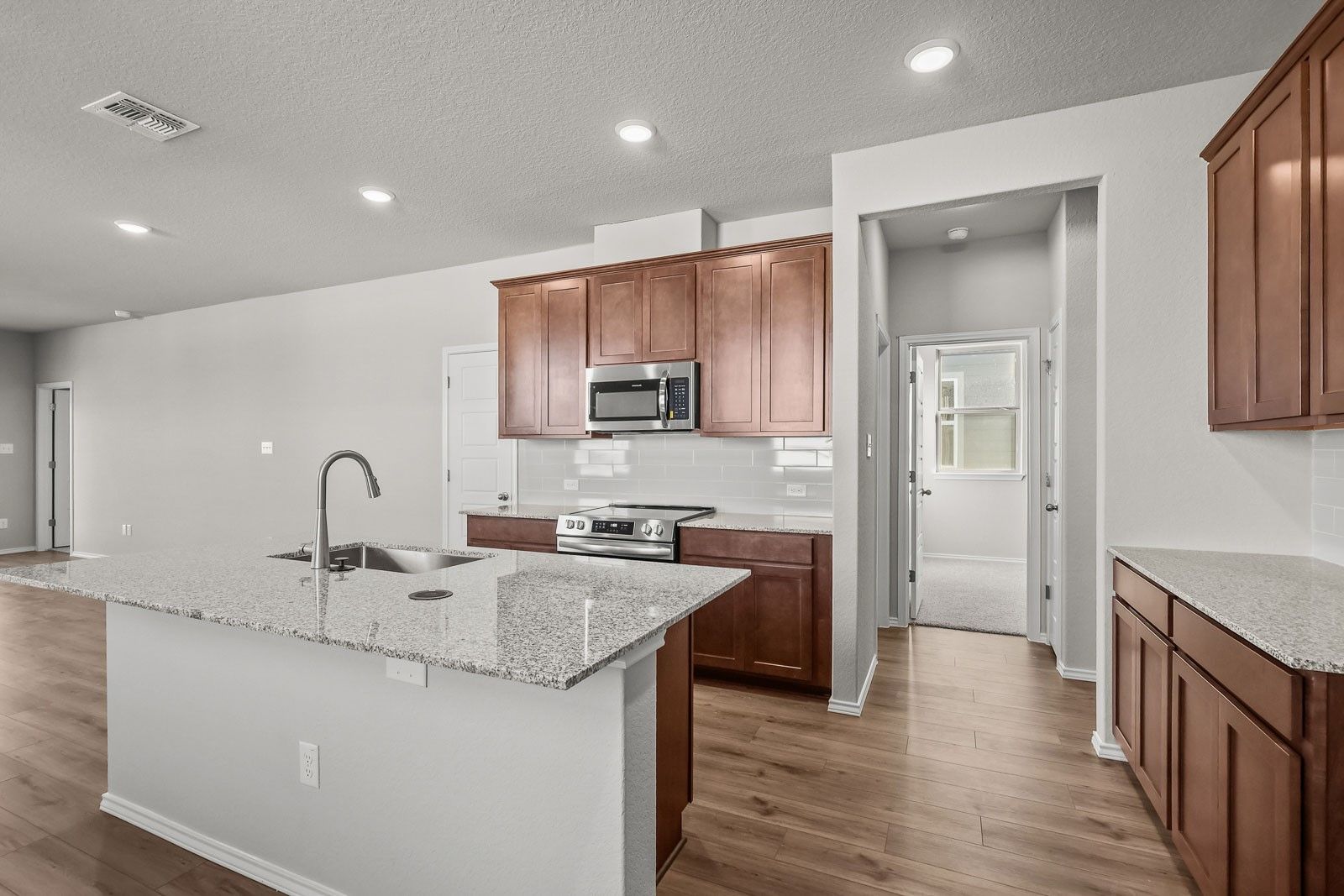 Modern kitchen with granite island and wood cabinets in The Frio G floor plan by Davidson Homes in Heartland, Texas.