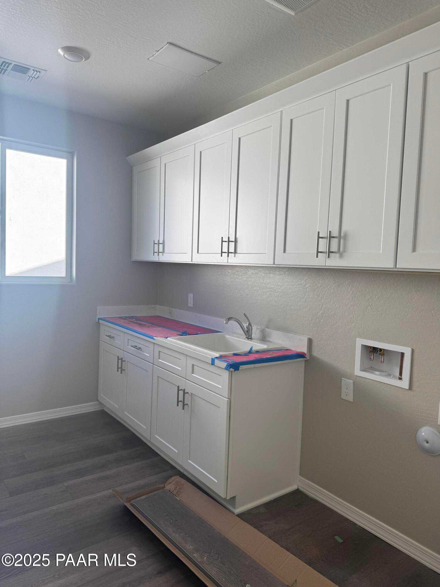 Modern laundry room with white shaker cabinets, utility sink, and washer hookup in Davidson Homes The Monarch E, Prescott, AZ