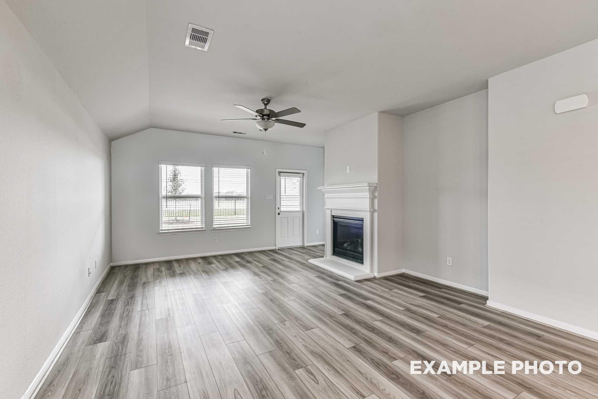Spacious living room with vaulted ceiling, ceiling fan, white gas fireplace, large windows, and luxury vinyl plank flooring in Davidson Homes The Riviera A, Rosharon, Texas
