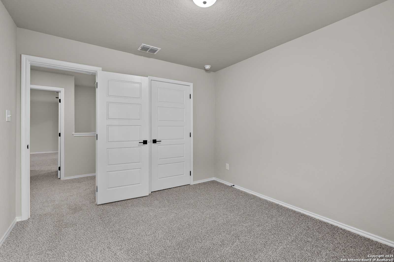 Spacious secondary bedroom featuring double closet doors, neutral beige walls, and carpet flooring in Davidson Homes The Murray I, San Antonio