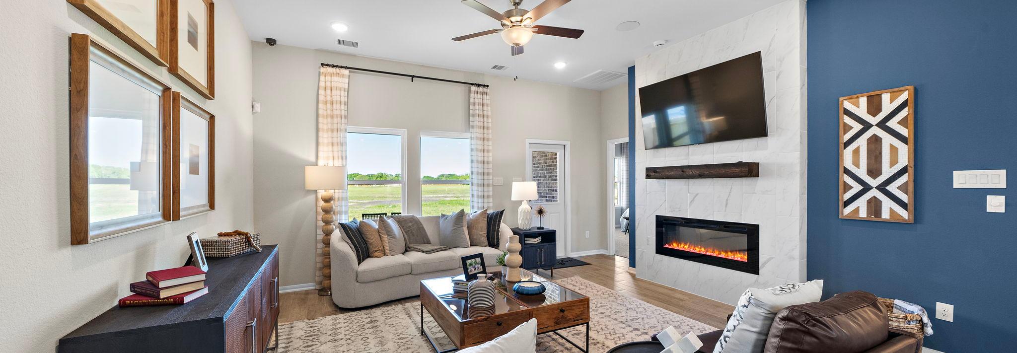 Open-concept living room in Emberly Beasley Texas with gray sectional sofa, gas fireplace, blue accent wall, hardwood floors