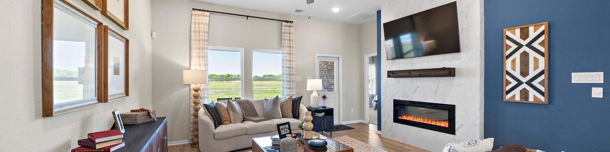 Open-concept living room in Emberly Beasley Texas with gray sectional sofa, gas fireplace, blue accent wall, hardwood floors