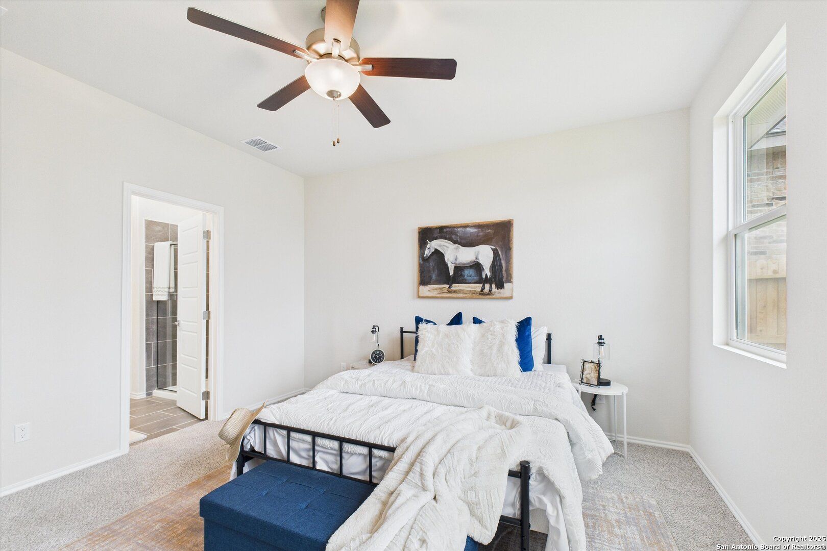 Cozy bedroom with white bedding, blue accents, ceiling fan, and horse wall art in Davidson Homes The Asheville K, Bricewood, San Antonio