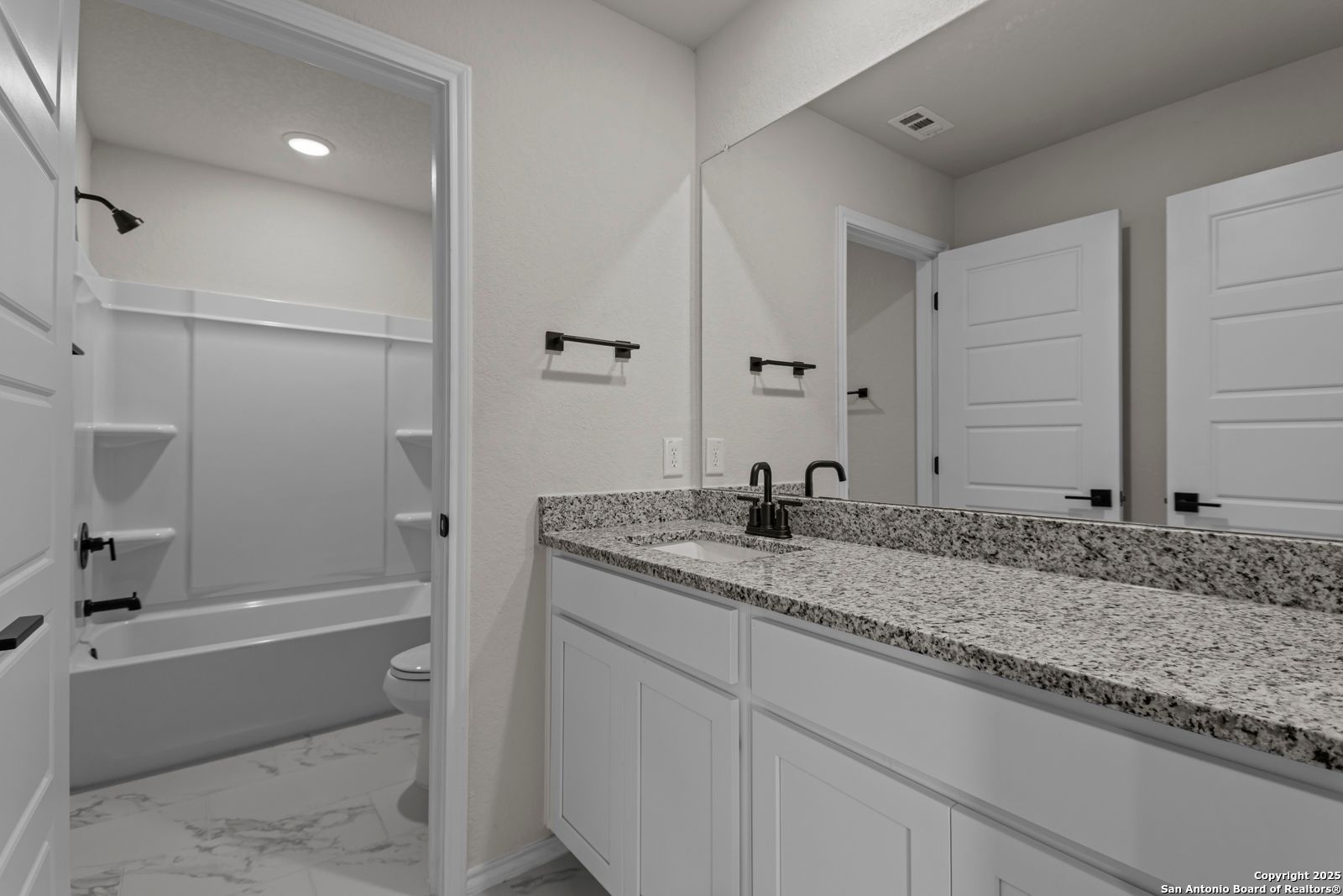 Modern bathroom with granite double vanity, black faucets, walk-in shower, and subway tile in Davidson Homes The Douglas C, Seguin, Texas