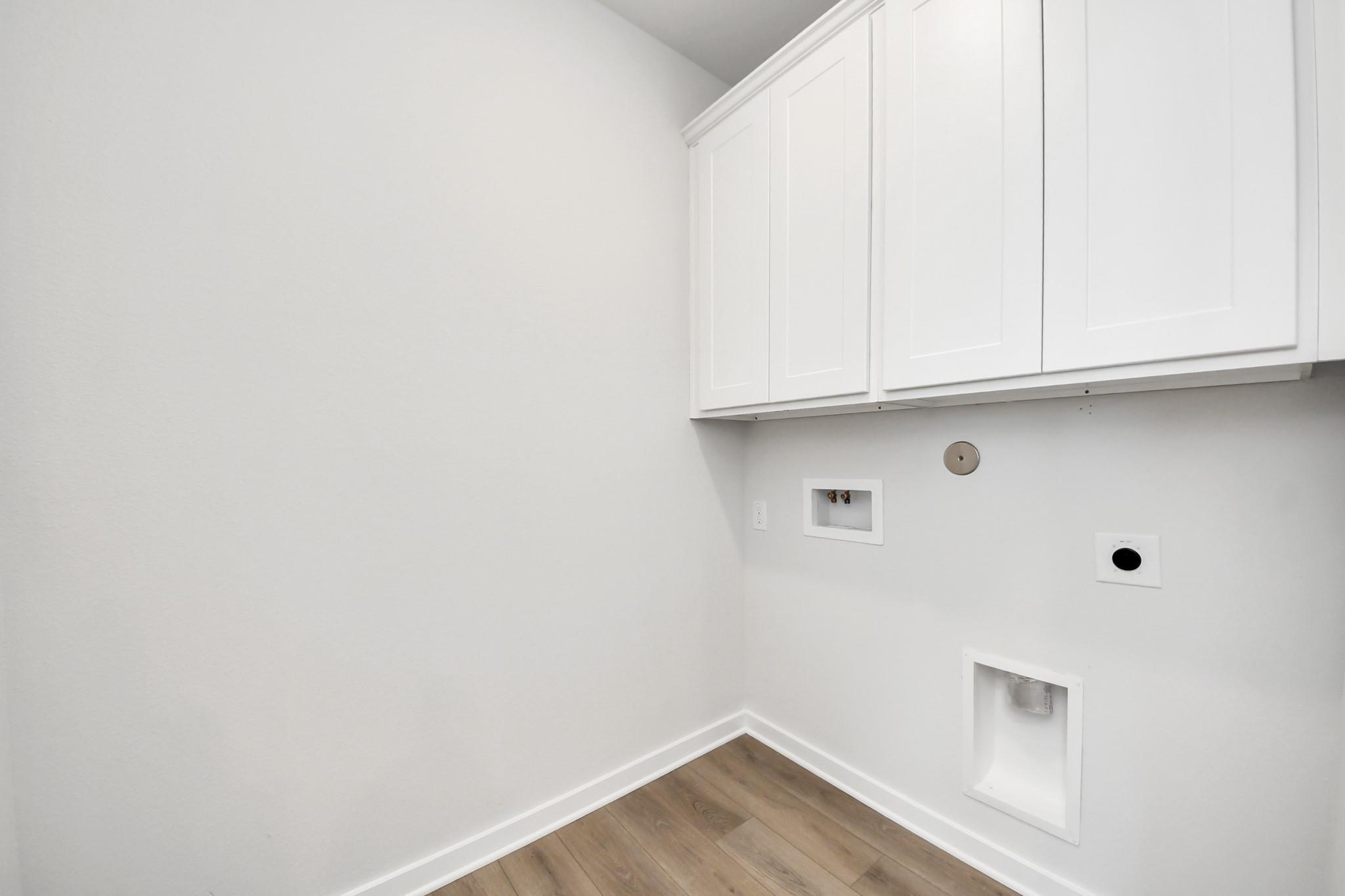 Utility room with white cabinets, wood-look flooring, and washer connections in The Costa A floor plan by Davidson Homes, Beasley, TX