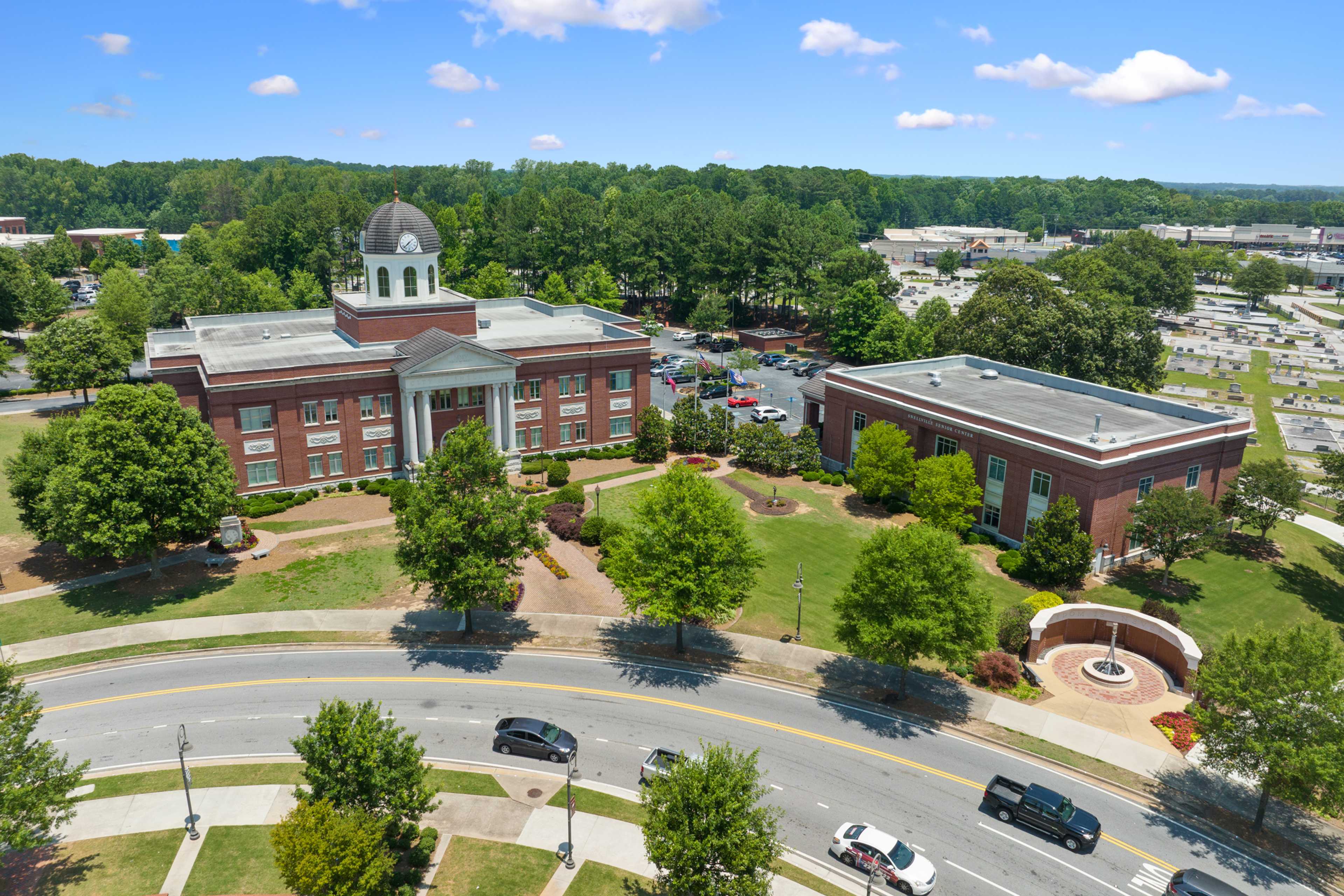 Aerial view of red brick courthouse with cupola dome and columns in Loganville Georgia near Kelly Preserve amid oak trees and parking lots