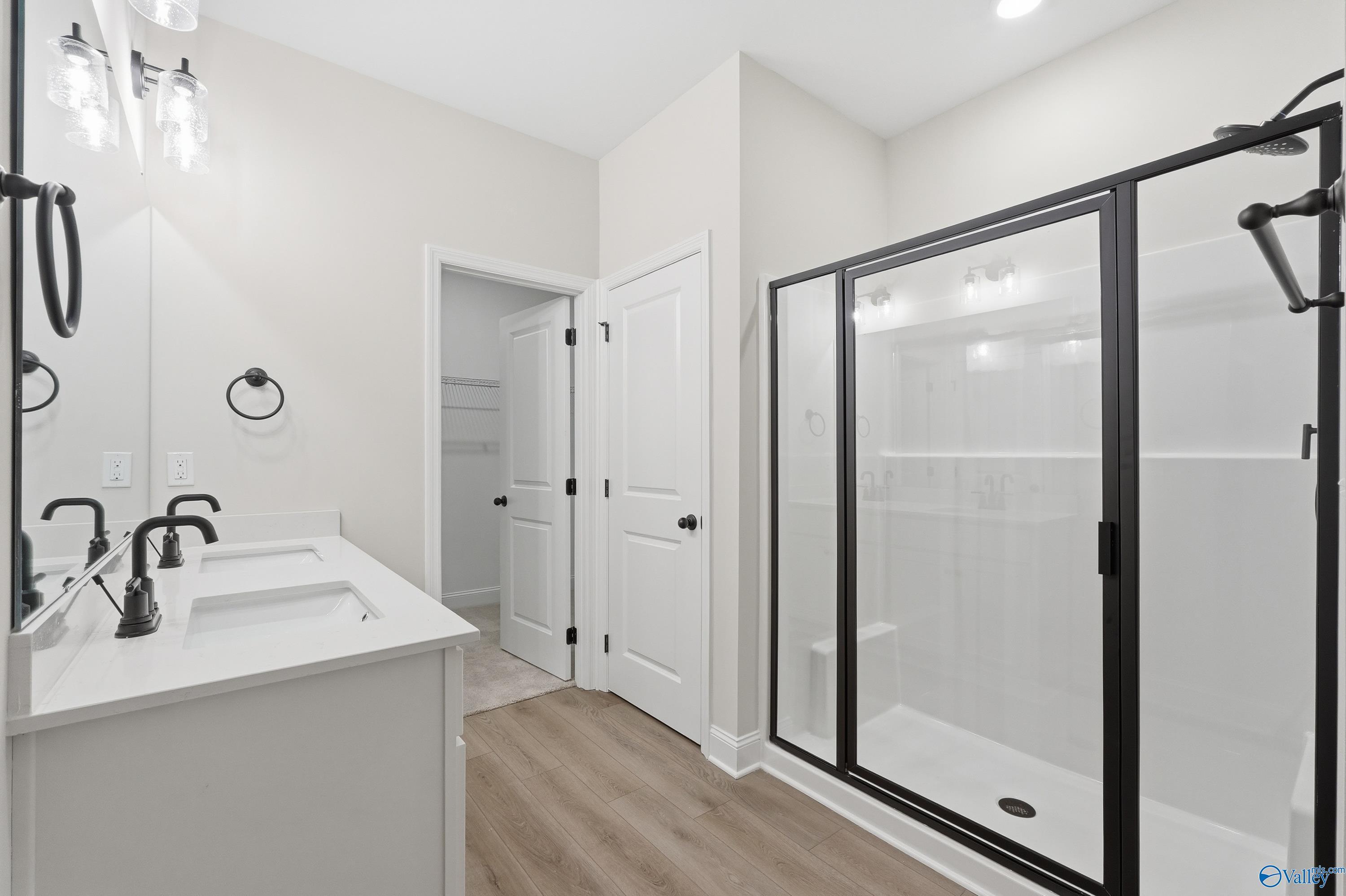 Modern master bathroom featuring double white quartz vanity, black faucets, glass shower enclosure, and linen closet in Davidson Homes The Franklin C, Meridianville, Alabama