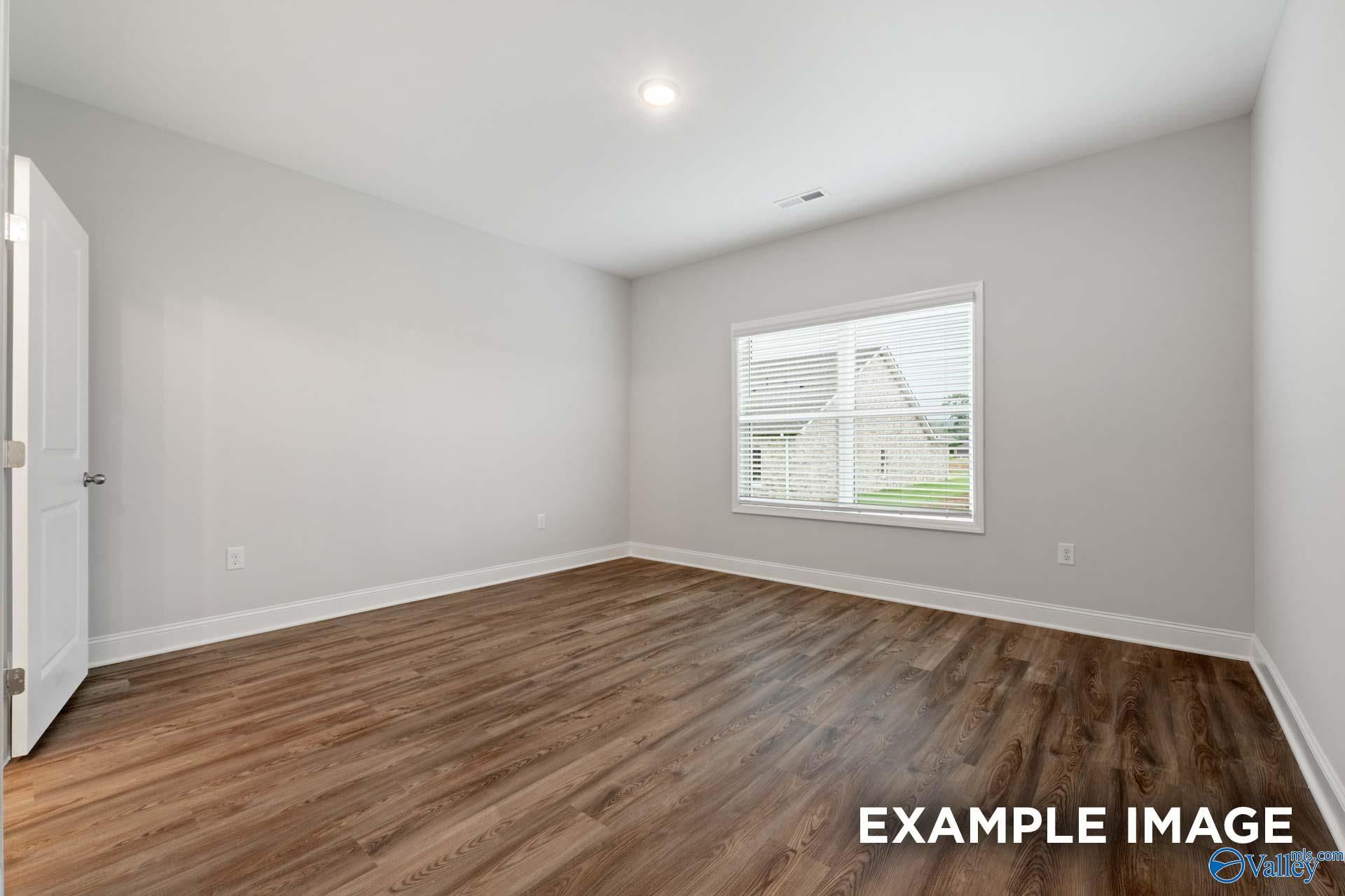 Bright secondary bedroom with light gray walls, hardwood floors, and window view in Davidson Homes The Cumberland, Decatur AL