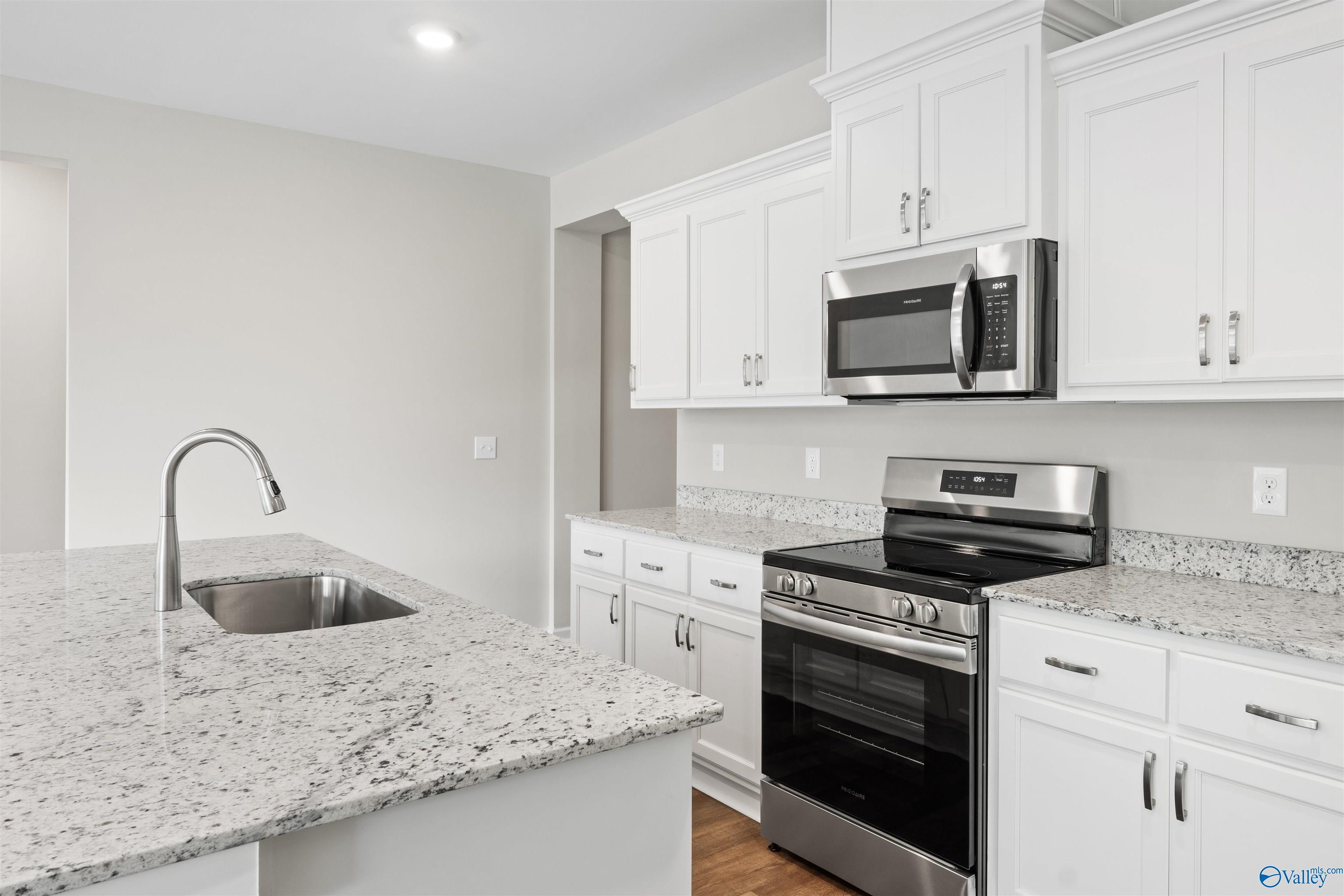 Modern kitchen with white shaker cabinets, granite island sink, stainless steel range in The Luna floor plan, Hazel Green, AL