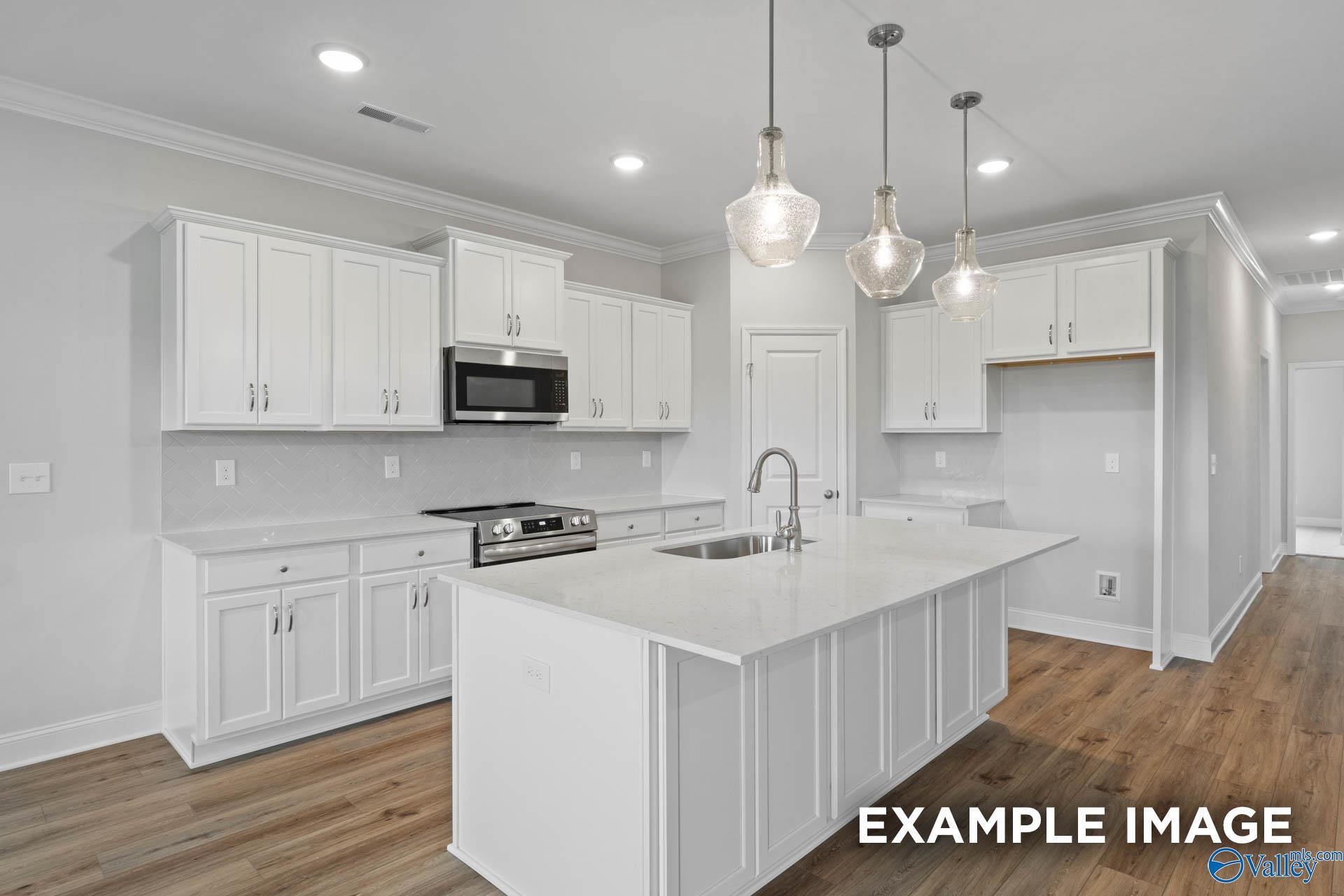 Modern kitchen with white cabinets, quartz island, and pendant lighting in The Rockford floor plan, Pikes Ridge, Alabama.