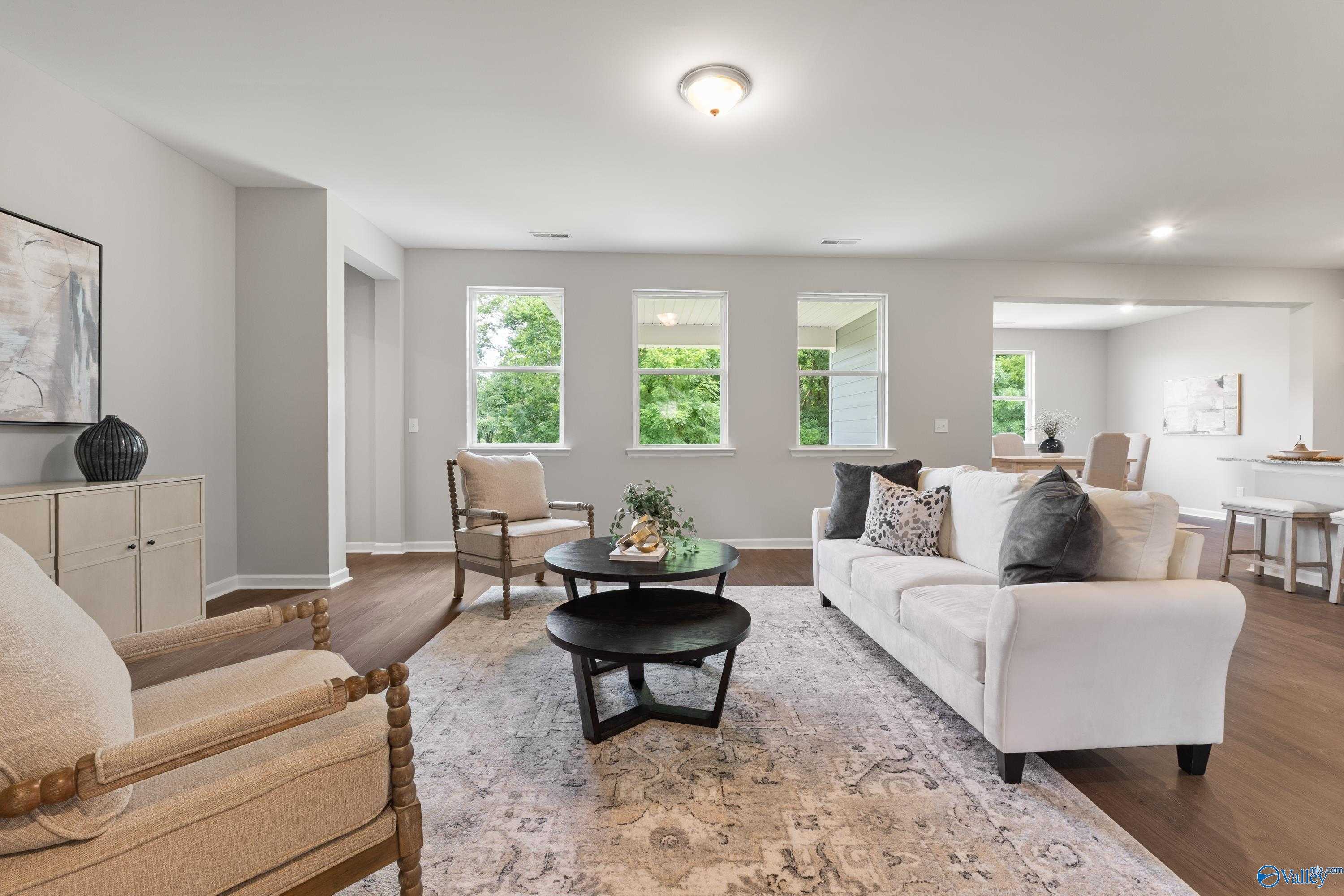 Spacious living room with white sectional sofa, armchairs, coffee table, and large windows in Davidson Homes The Avalon, Huntsville