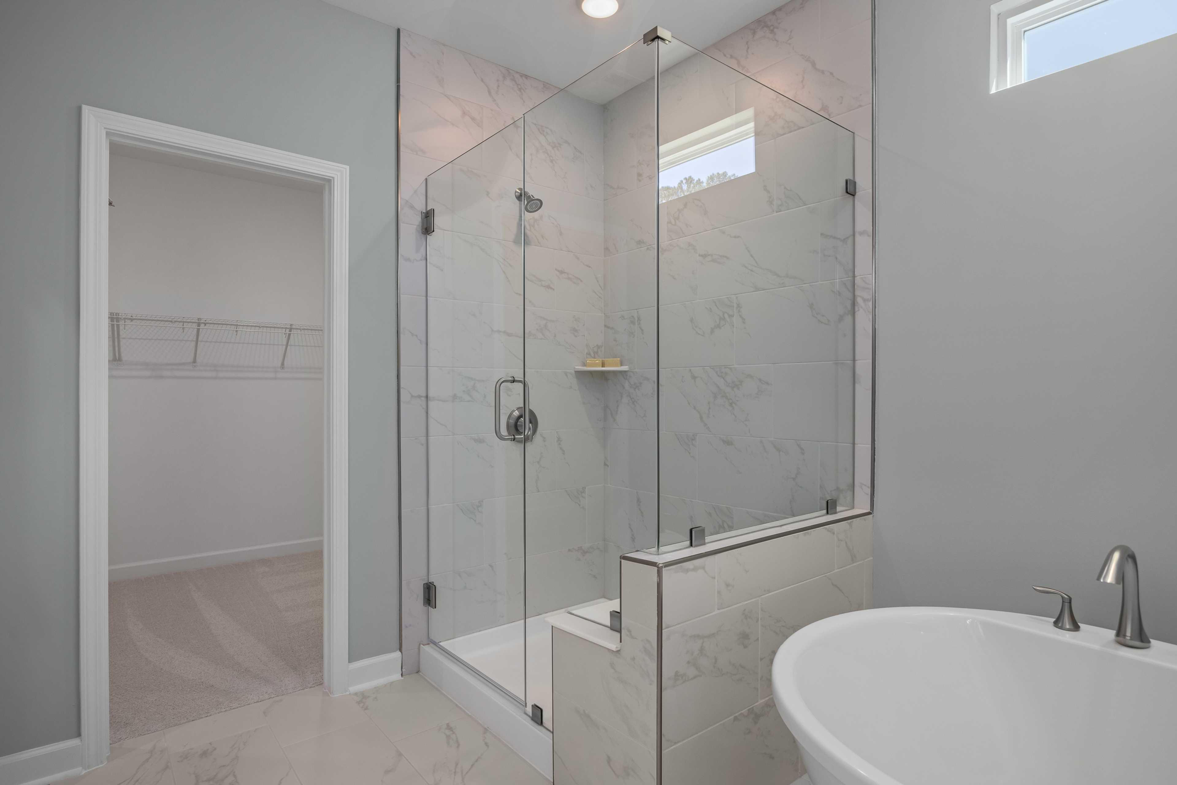 Luxury primary bathroom at Sage on North Main in Wake Forest NC with frameless glass shower, marble tiles, freestanding tub