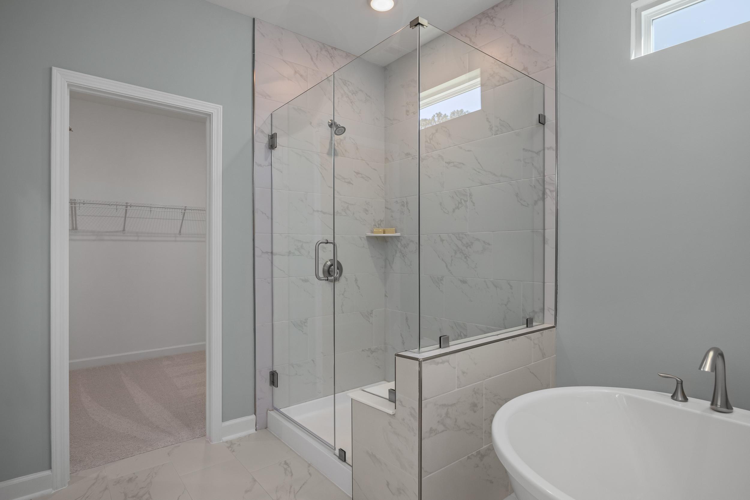 Modern master bathroom in The Hickory II featuring frameless glass shower, marble tile walls, and freestanding tub