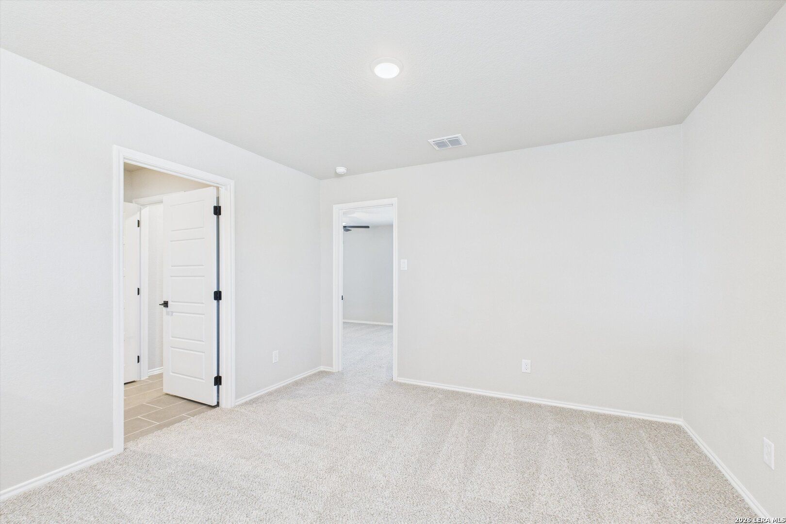 Spacious secondary bedroom with neutral white walls, beige carpet, and arched doorways in Davidson Homes The Charlotte A, San Antonio