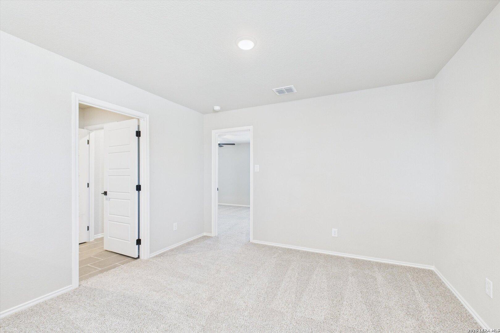 Spacious secondary bedroom with neutral white walls, beige carpet, and arched doorways in Davidson Homes The Charlotte A, San Antonio
