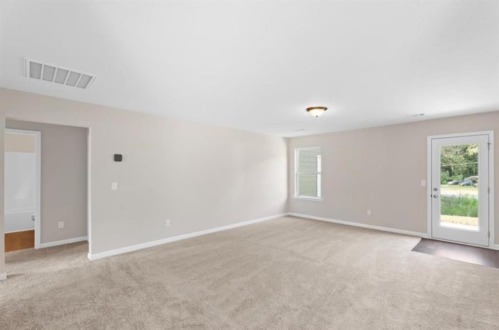 Empty living room with beige walls, carpet flooring, backyard view through glass door in The Washington 3-bedroom home, Phenix City, Alabama