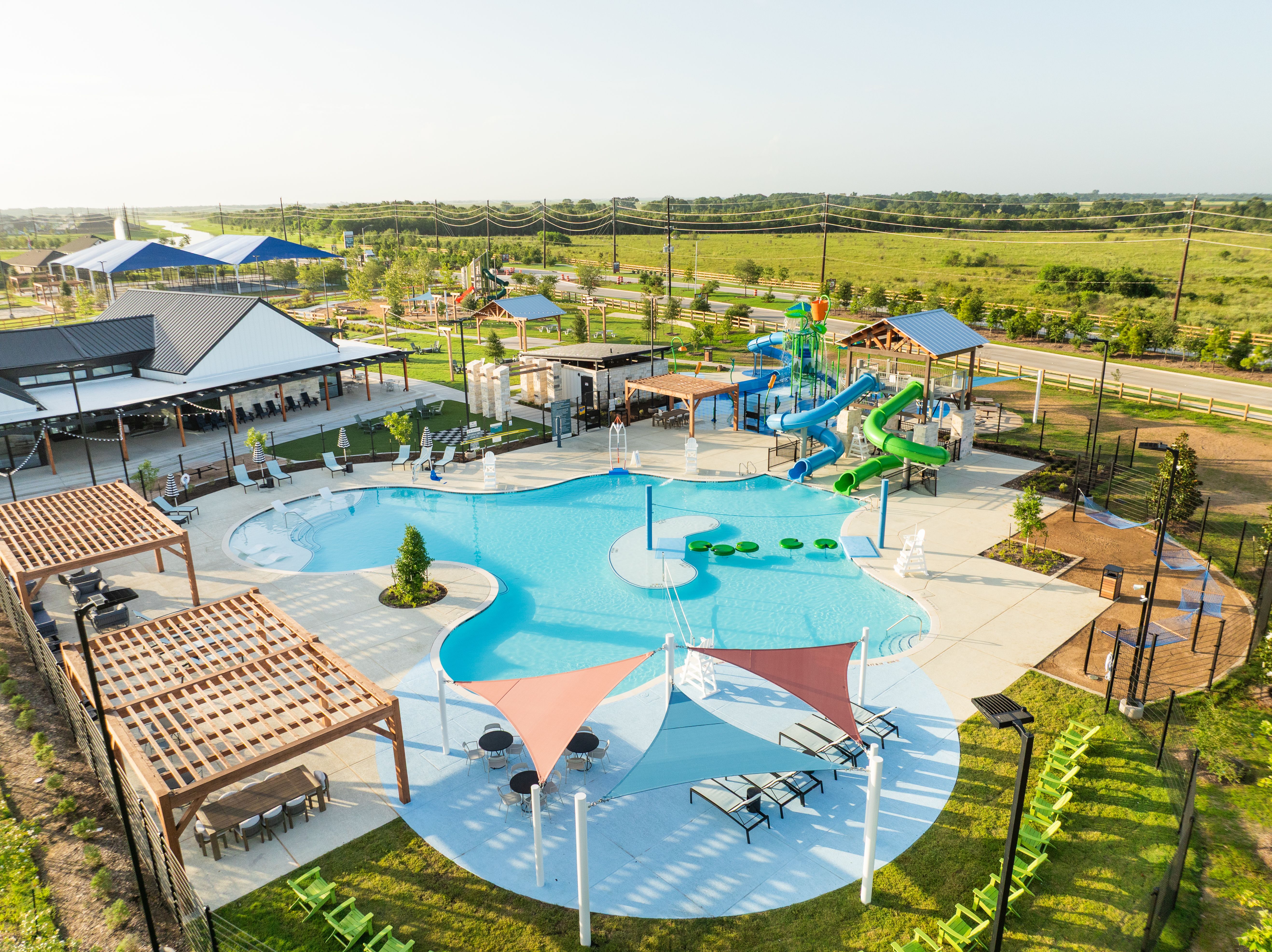 Resort-style pool at Emberly in Beasley Texas with water slides, shaded lounges, and pergolas
