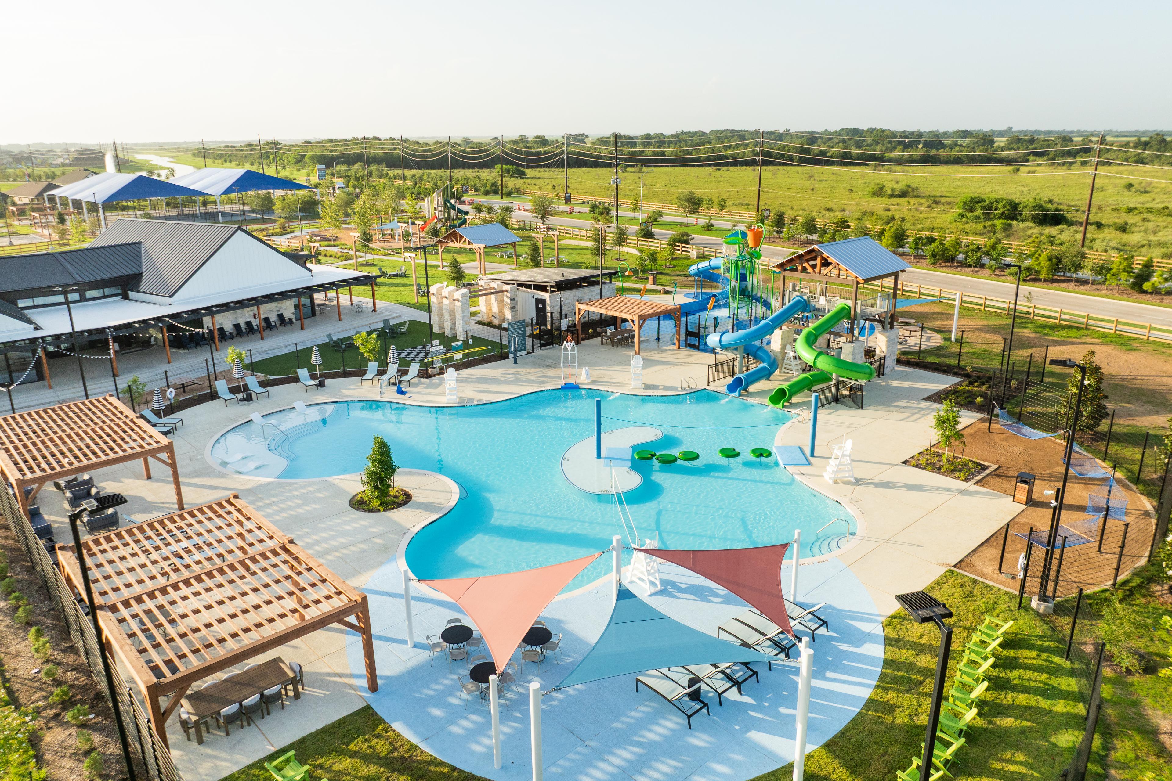 Resort-style pool at Emberly in Beasley Texas with water slides, shaded lounges, and pergolas