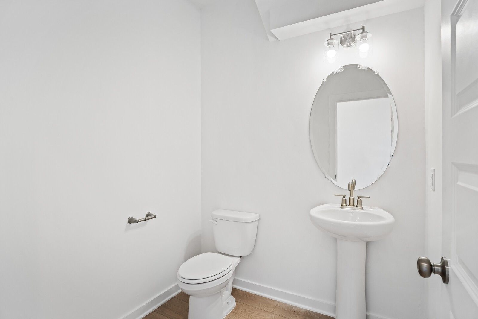 Elegant powder room featuring pedestal sink, round mirror, toilet and soft lighting in Davidson Homes The Logan B, Calista Farms, White House, TN