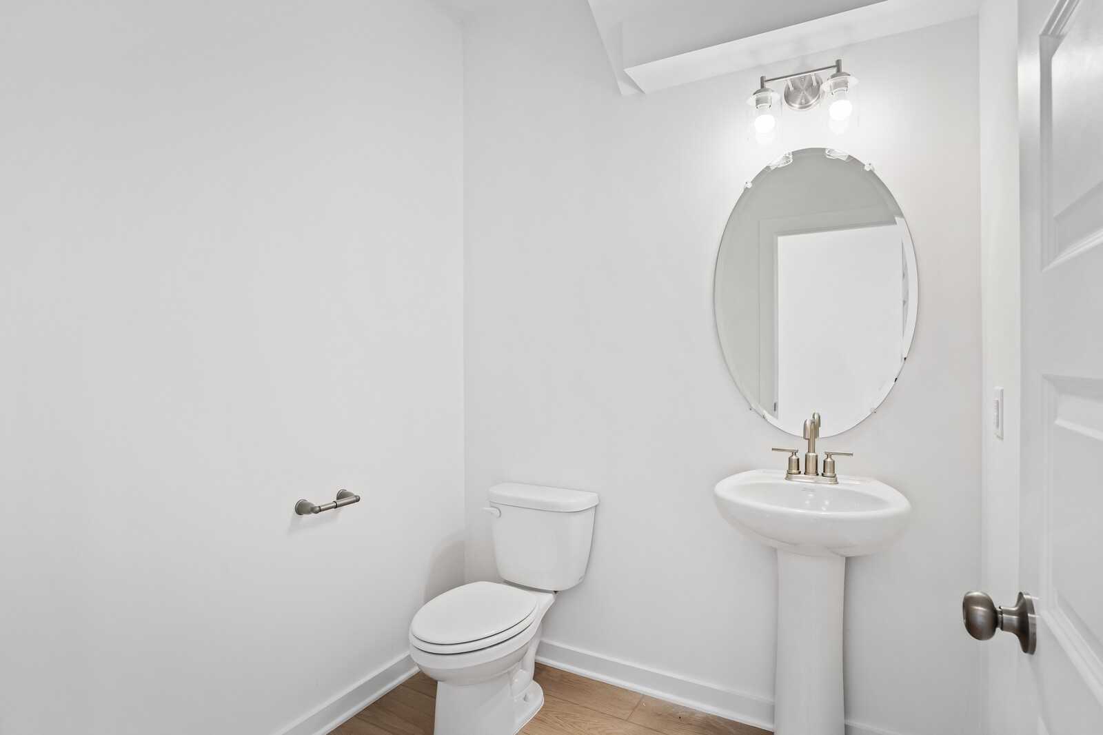 Elegant powder room featuring pedestal sink, round mirror, toilet and soft lighting in Davidson Homes The Logan B, Calista Farms, White House, TN