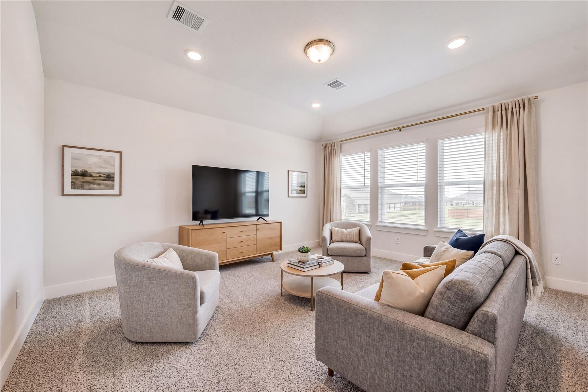 Modern living room with gray sofa, armchairs, mounted TV, large windows in Davidson Homes The Victoria A, Lago Mar, Texas City
