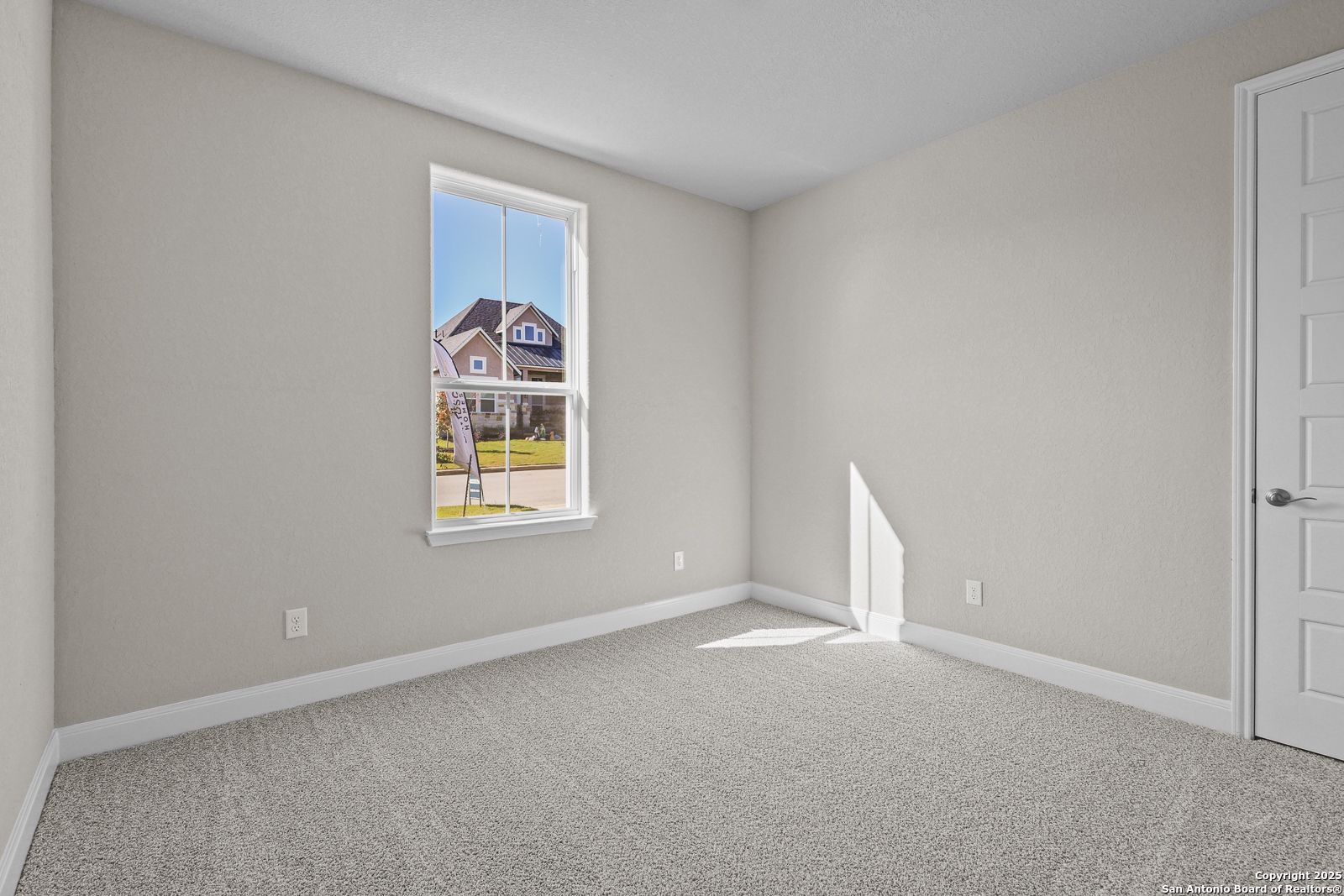 Bright secondary bedroom with neutral walls, carpet flooring, and window view of neighborhood in Davidson Homes The Jennings G, Castroville, Texas