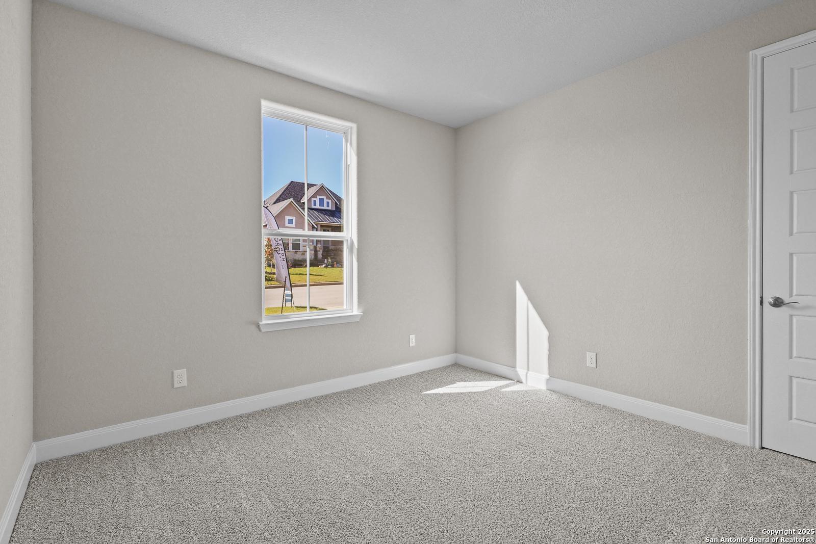 Bright secondary bedroom with neutral walls, carpet flooring, and window view of neighborhood in Davidson Homes The Jennings G, Castroville, Texas