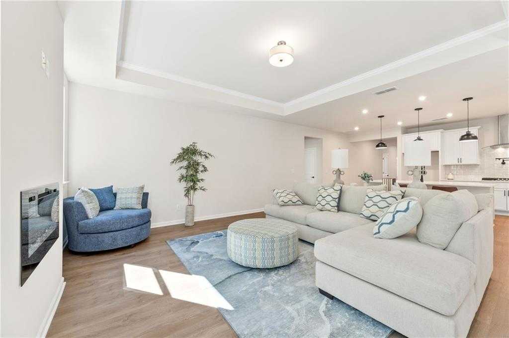 Cozy modern living room with gray sectional sofa, blue armchair, electric fireplace, and open kitchen in The Daphne B 4-bedroom home, Loganville, Georgia